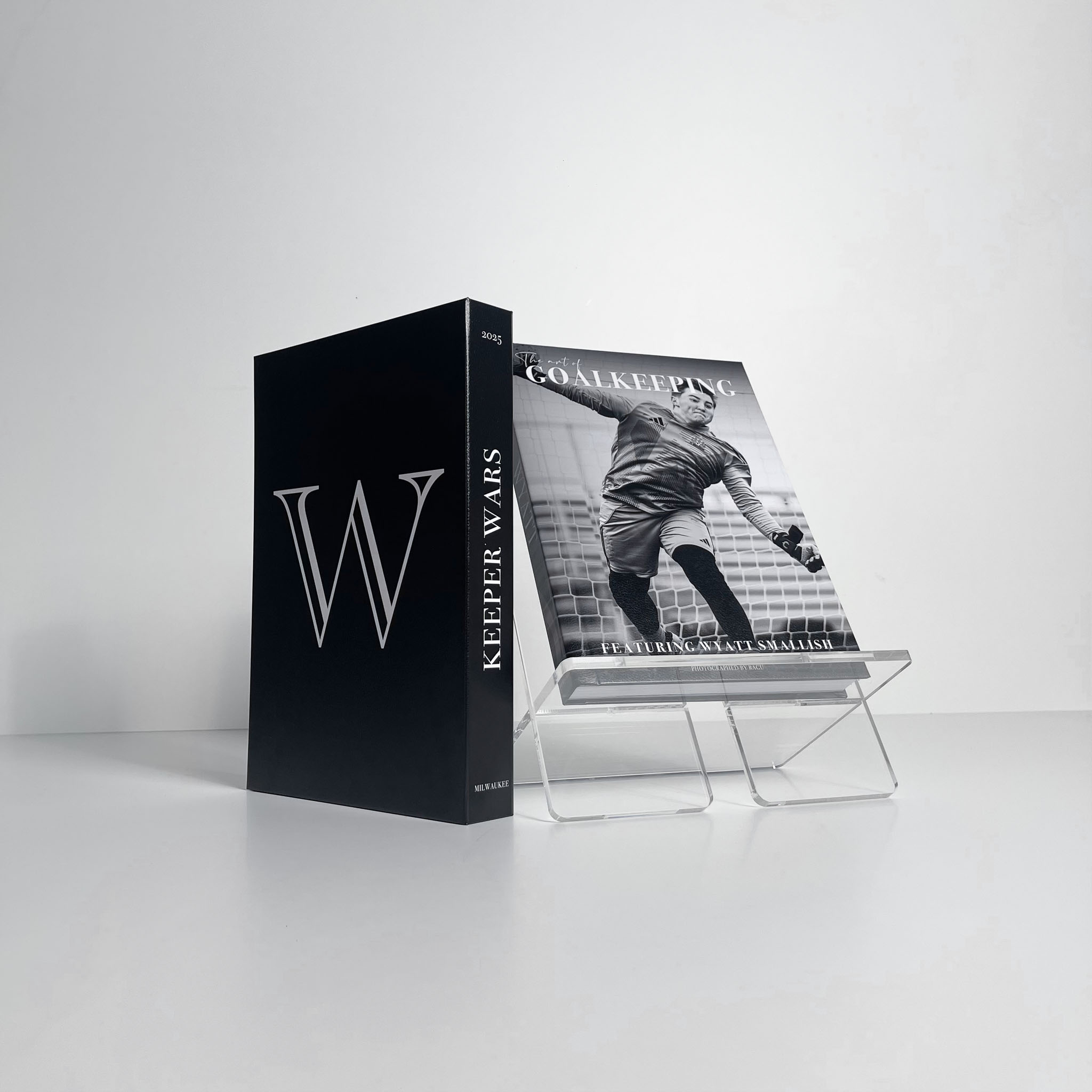 A fine-art Athlete Book showing a goalkeeper in action rests on a clear acrylic stand, with its matching book case standing elegantly beside it.