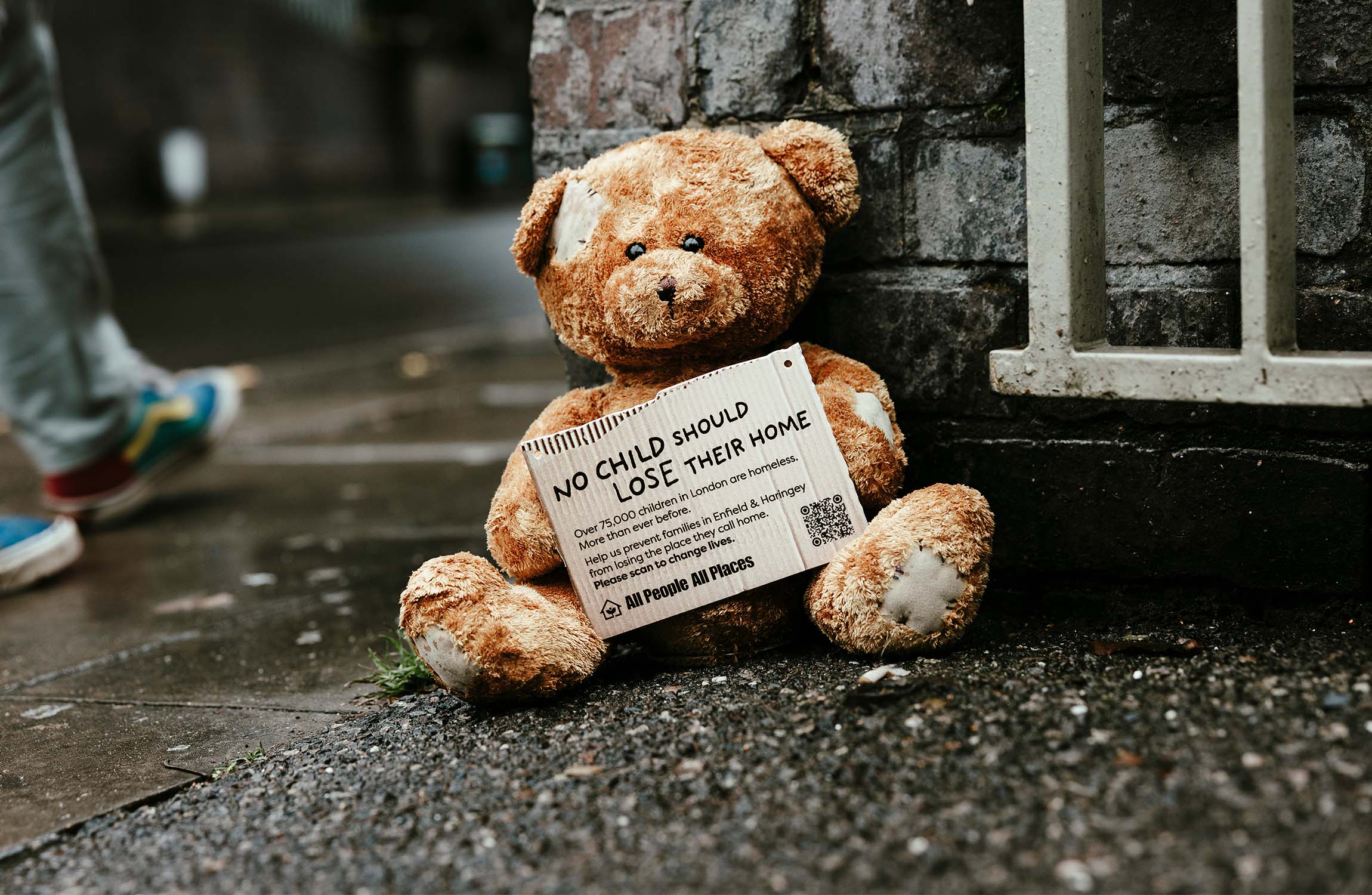 Stuffed Teddy bear toy on a wet pavement holding a sign that says No Child should loose their home