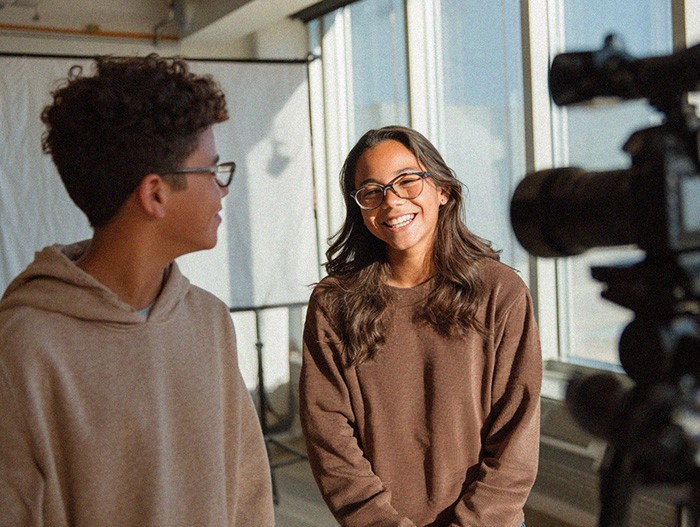 Student smiling while talking with a classmate in a bright indoor space.