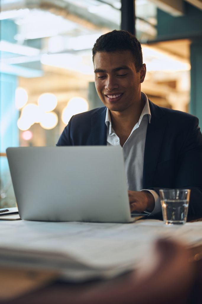 Man wearing headphones and a white t-shirt working on a laptop in soft natural light, with window shadows cast on the wall.