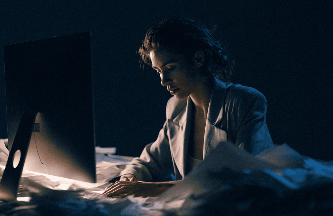 Mulher trabalhando concentrada em frente ao computador em uma sala escura à noite.