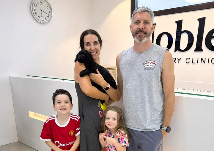 Family of four with a black puppy smiling at the Noble reception desk.