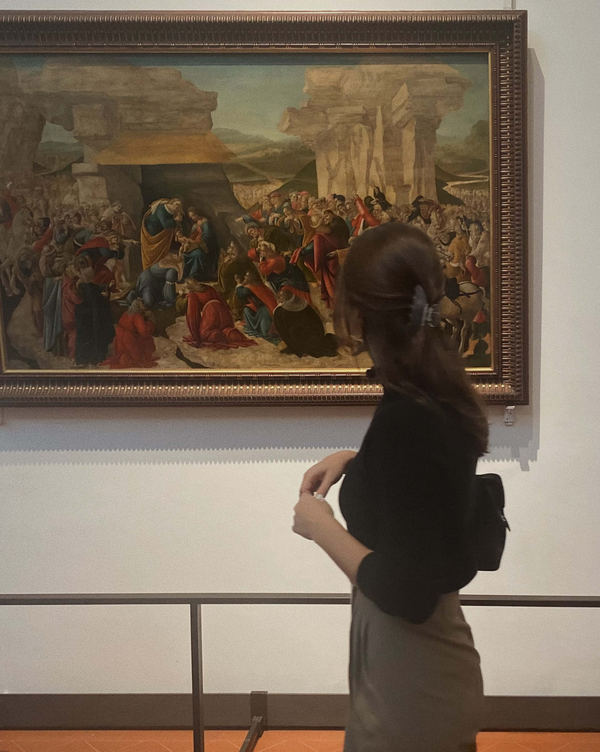 a young woman in a black turtleneck and grey slacks standing in front of a renaissance painting in a museum