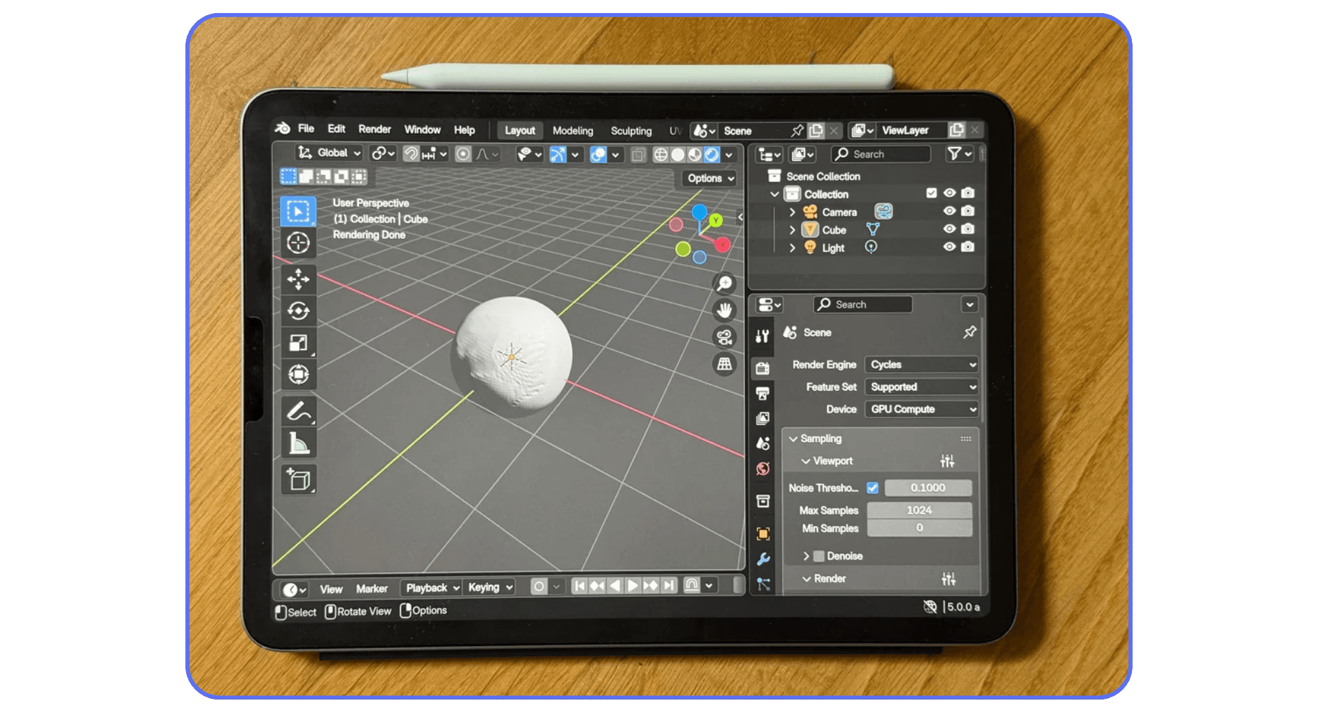 iPad showing Blender interface with a simple 3D sphere on a grid workspace, labeled as “User Perspective.” The Apple Pencil rests on top of the tablet.