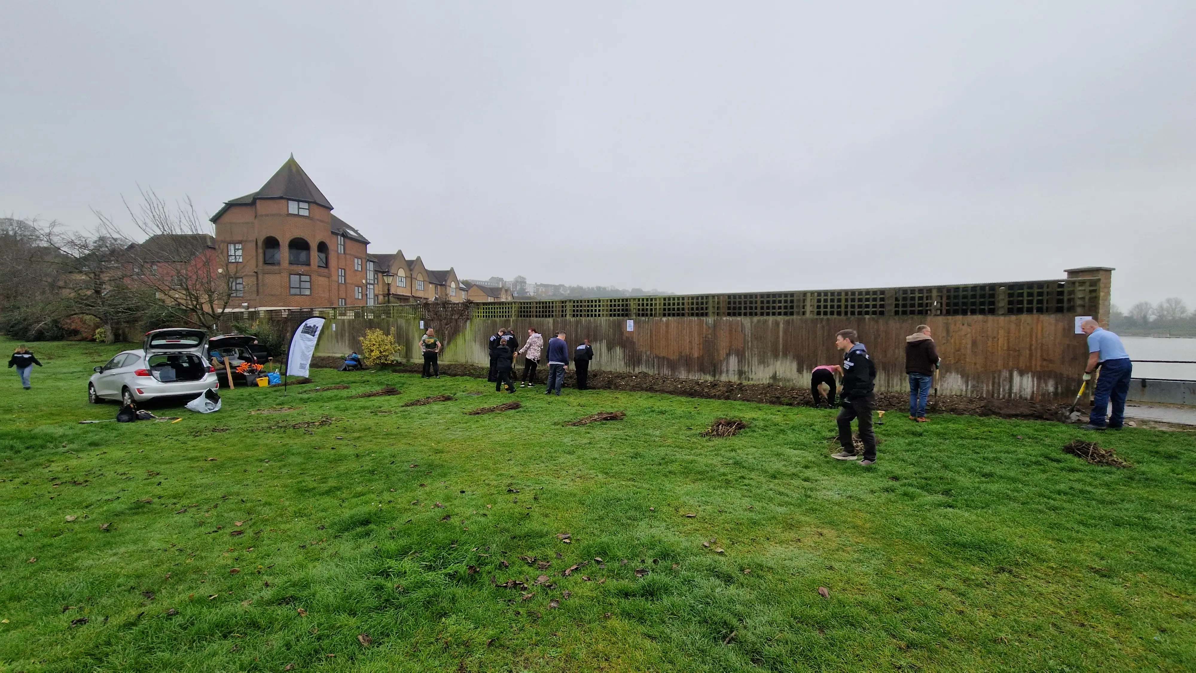 A group of people working near a wooden structure on a grassy field, with a cloudy sky in the background.