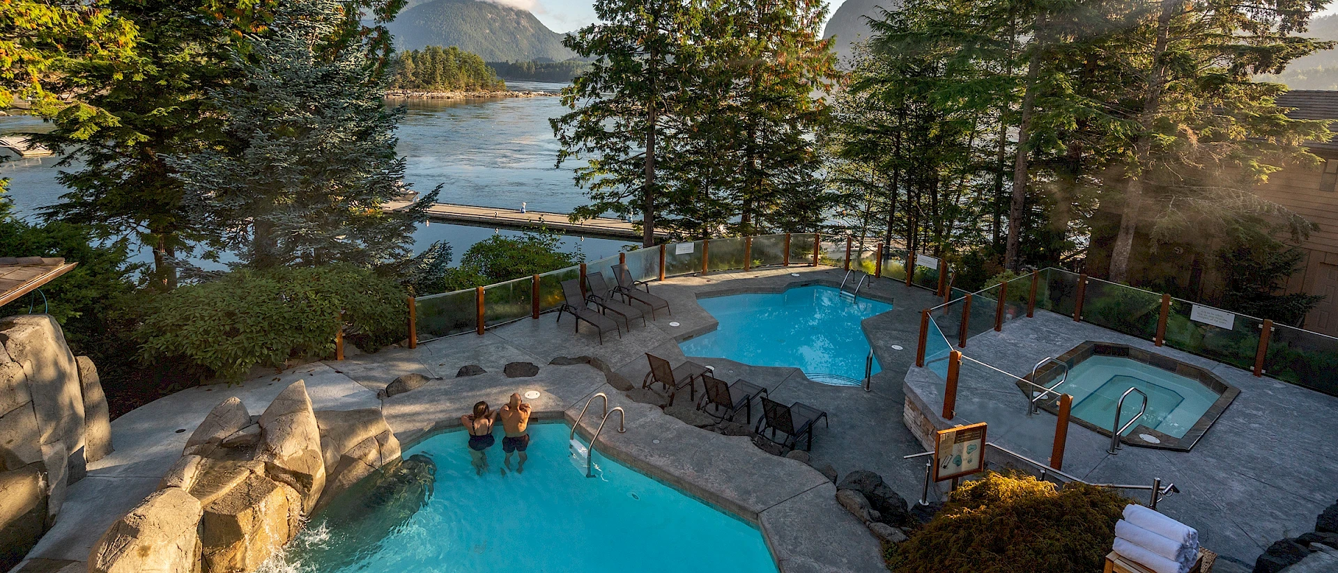 Luftaufnahme eines weitläufigen Luxus-Resorts an einer Meeresbucht mit modernen Bungalows, zwei großen blauen Außenpools und direktem Zugang zum Sandstrand.