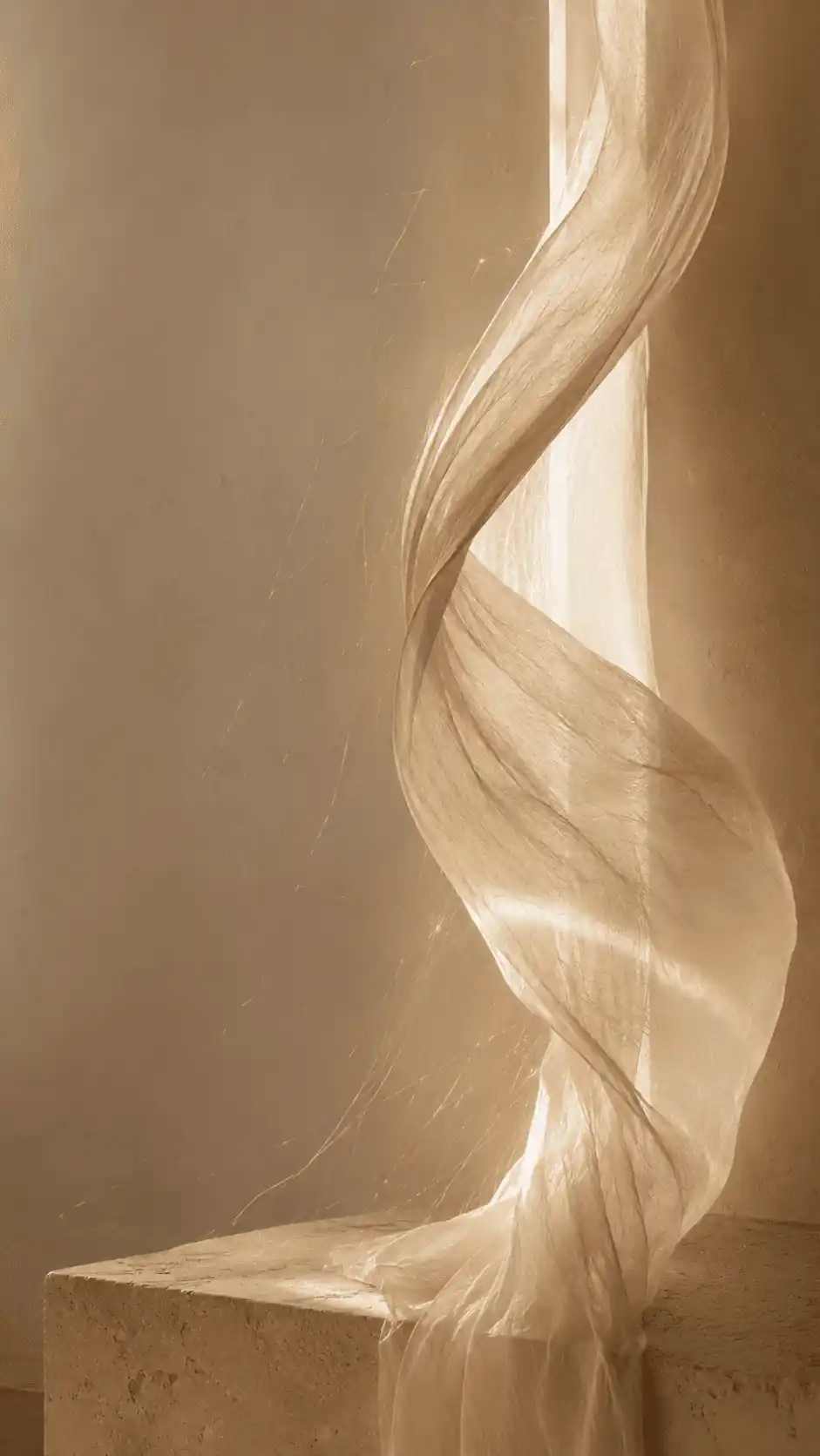 Sheer fabric curling upward in warm light above a stone plinth
