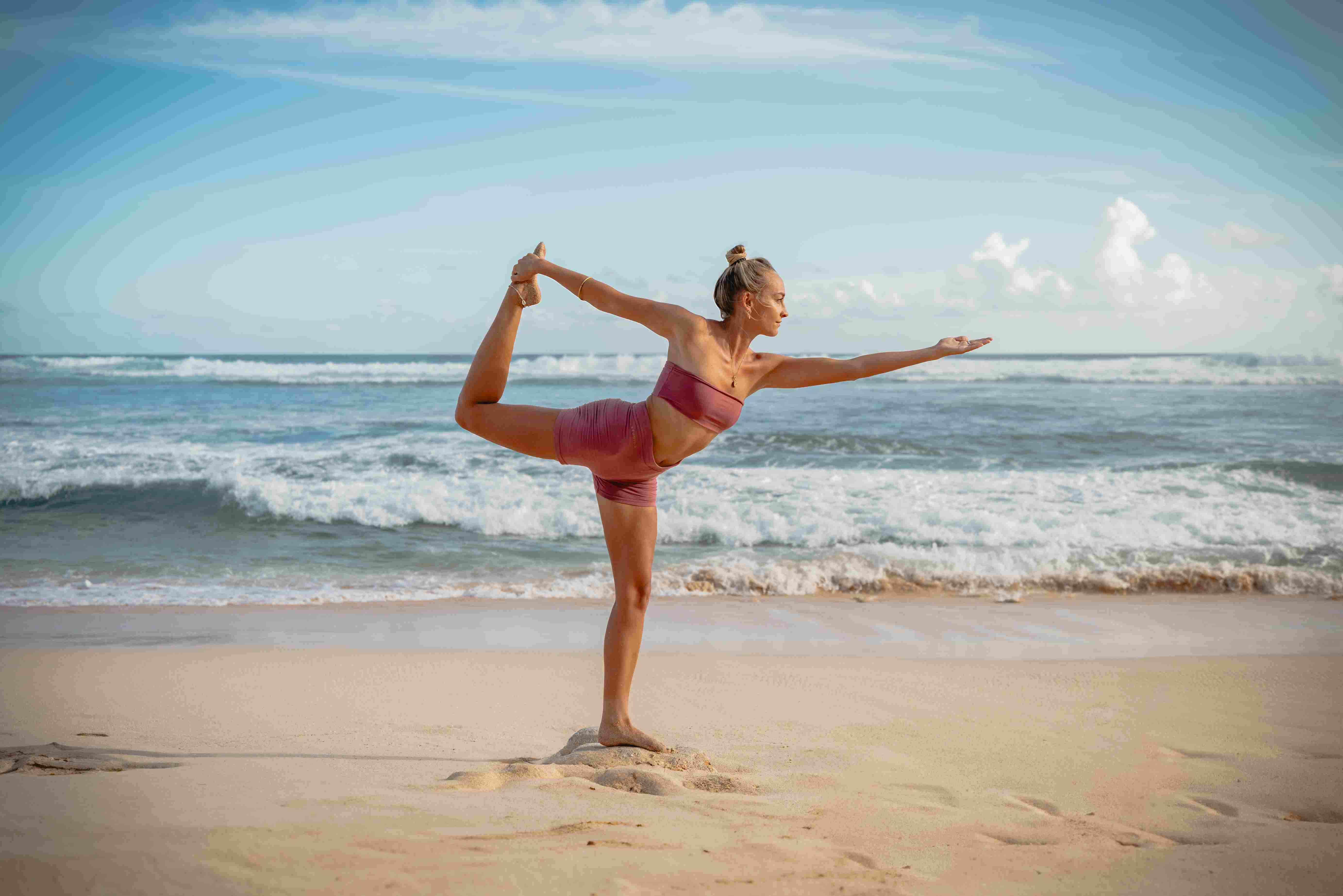 Woman practicing Lord of the Dance pose (Natarajasana) on the beach with ocean background in Bali.