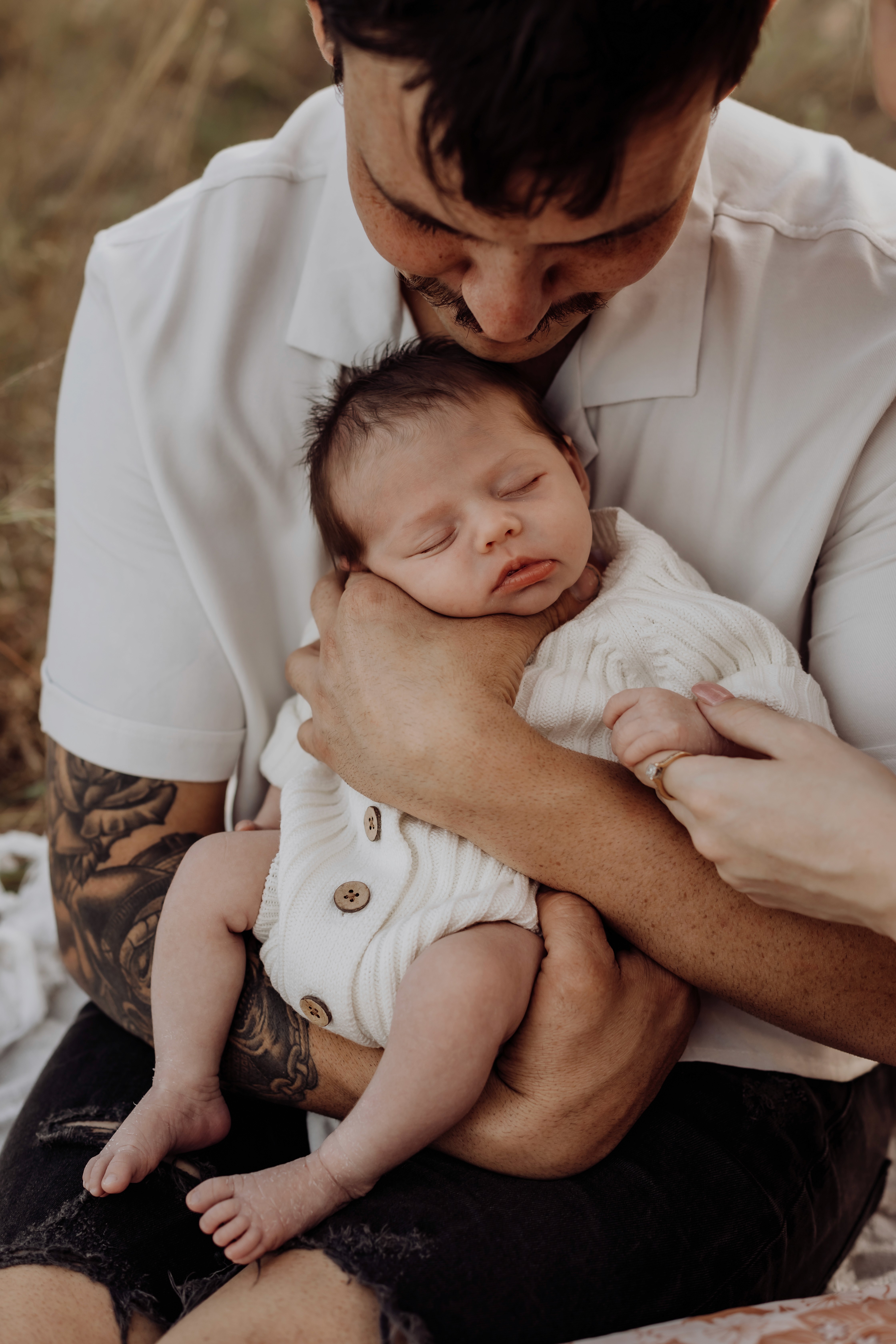 Parents holding sleeping baby while sitting in the long grass in Mackay