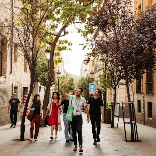 קבוצה של אנשים הולכת ברחוב עם עצים בשני הצדדים ומבנים משני צדדים, כאשר אדם אחד מצביע כלפי מעלה.