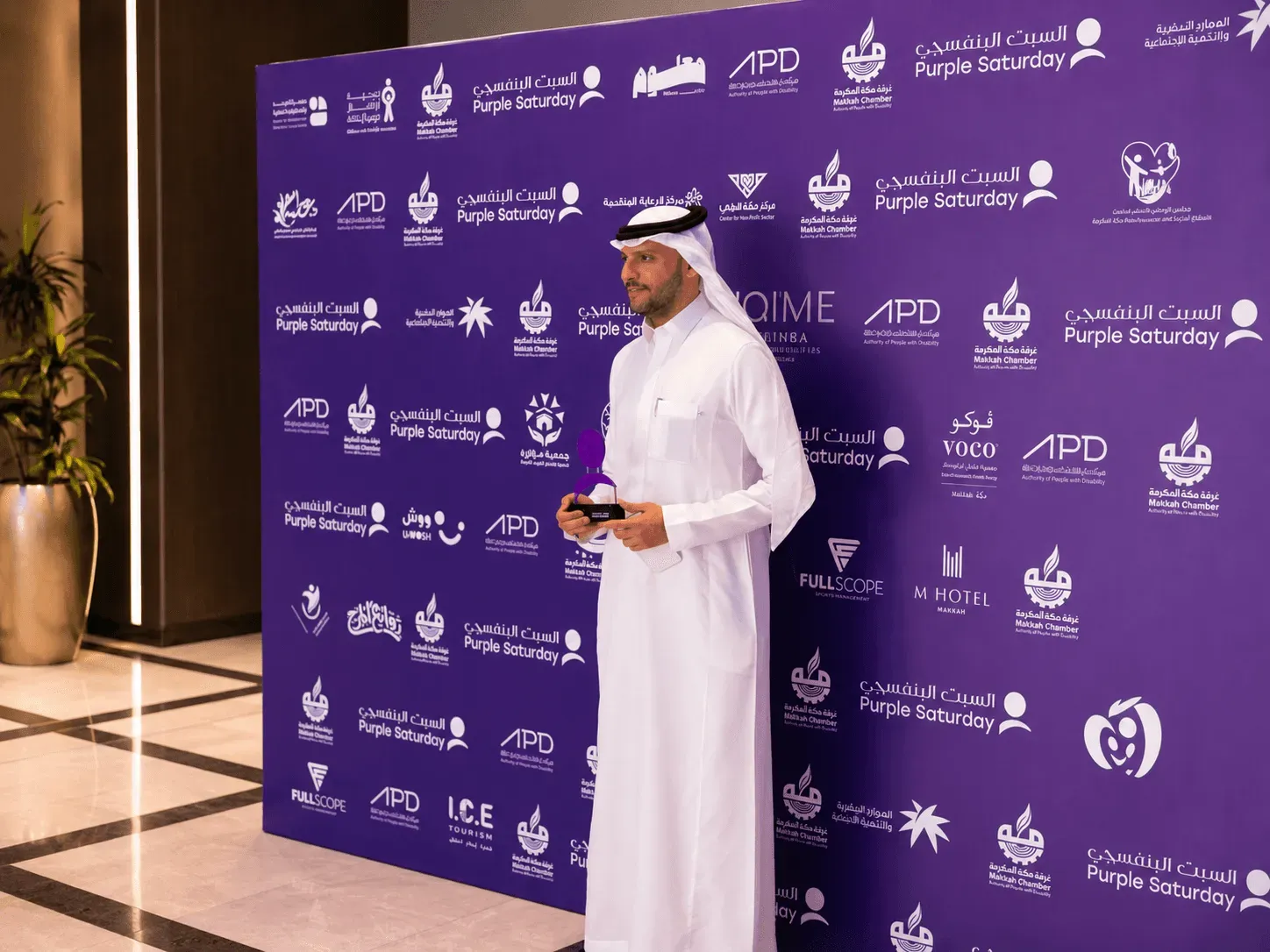 Guest standing in front of the Purple Saturday sponsor photo backdrop