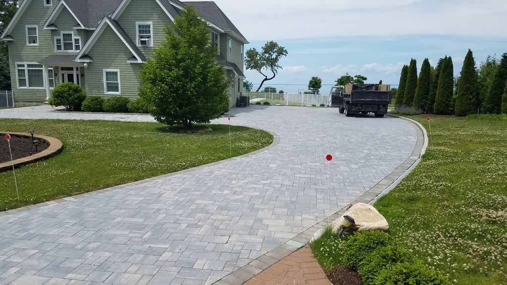 gray curved brick driveway with green house and greenery