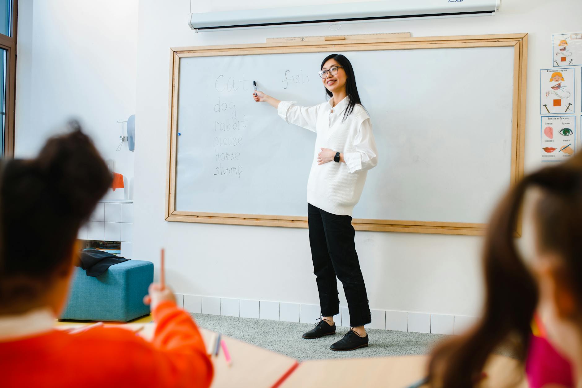 A science teacher in a white lab coat demonstrates a chemical reaction using colorful liquids in glass beakers.