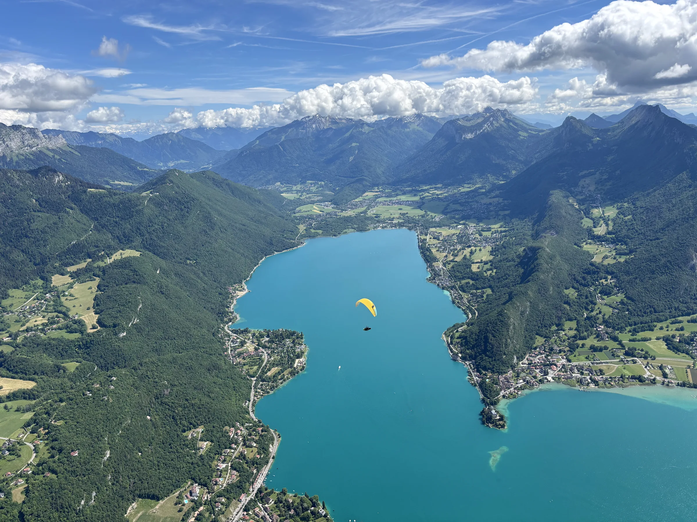 Yellow paraglider flying above Lake Annecy and mountain ridges