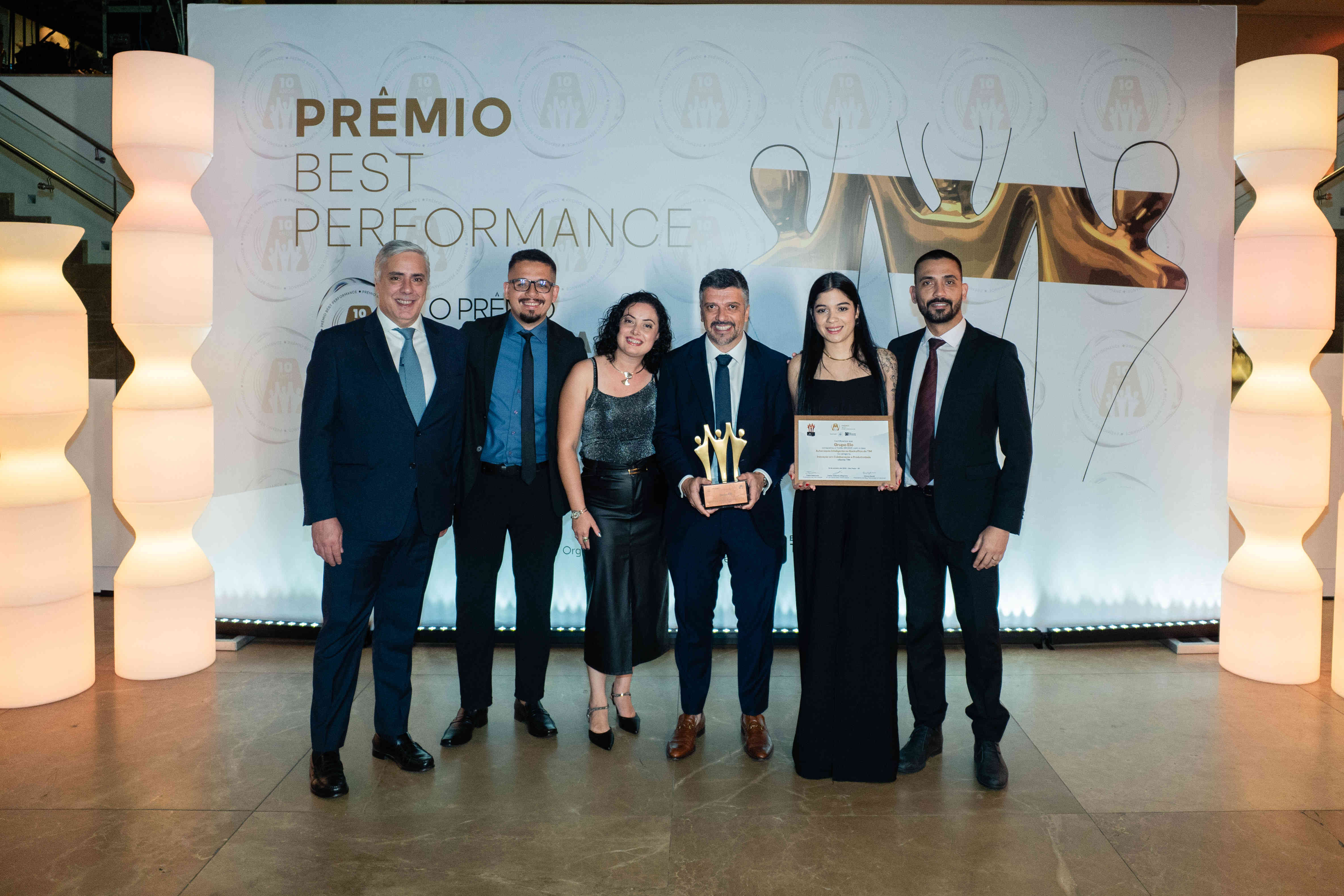 Executivos do Grupo Elo posando com troféu bronze e certificado no palco do Prêmio Best Performance 2025.