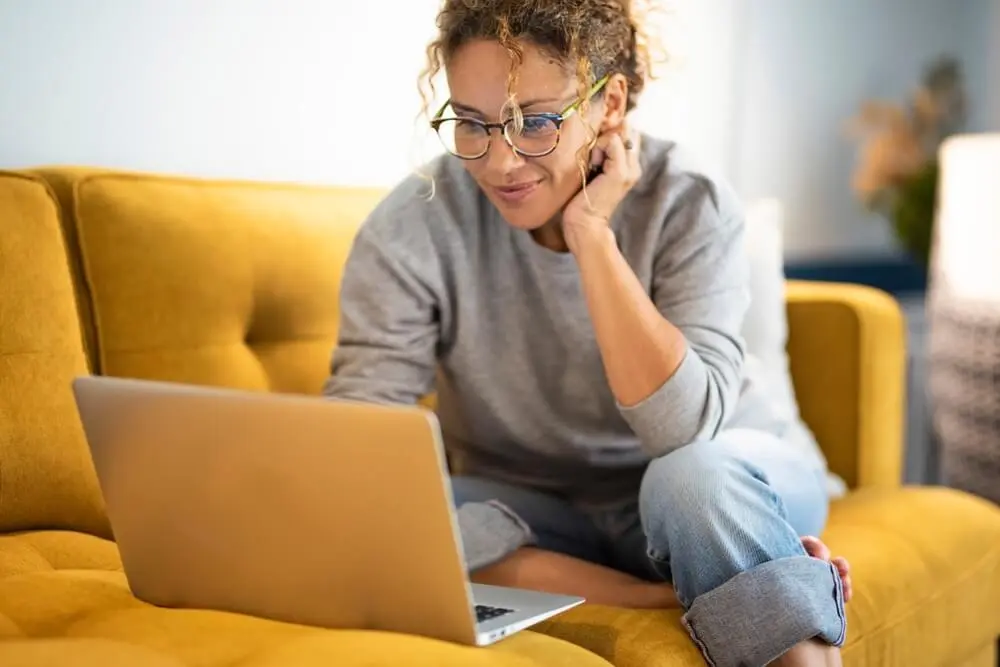 Woman sitting on a yellow sofa using a laptop and smiling