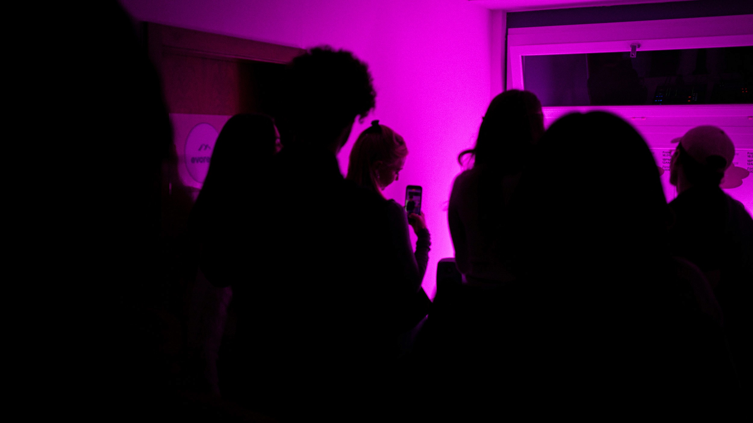 Candid silhouettes of guests enjoying drinks against a saturated pink neon background at the studio housewarming. This atmospheric shot captures the vibrant energy of the event, showcasing the studio's vibrant internal culture and its connection to the local creative scene.
