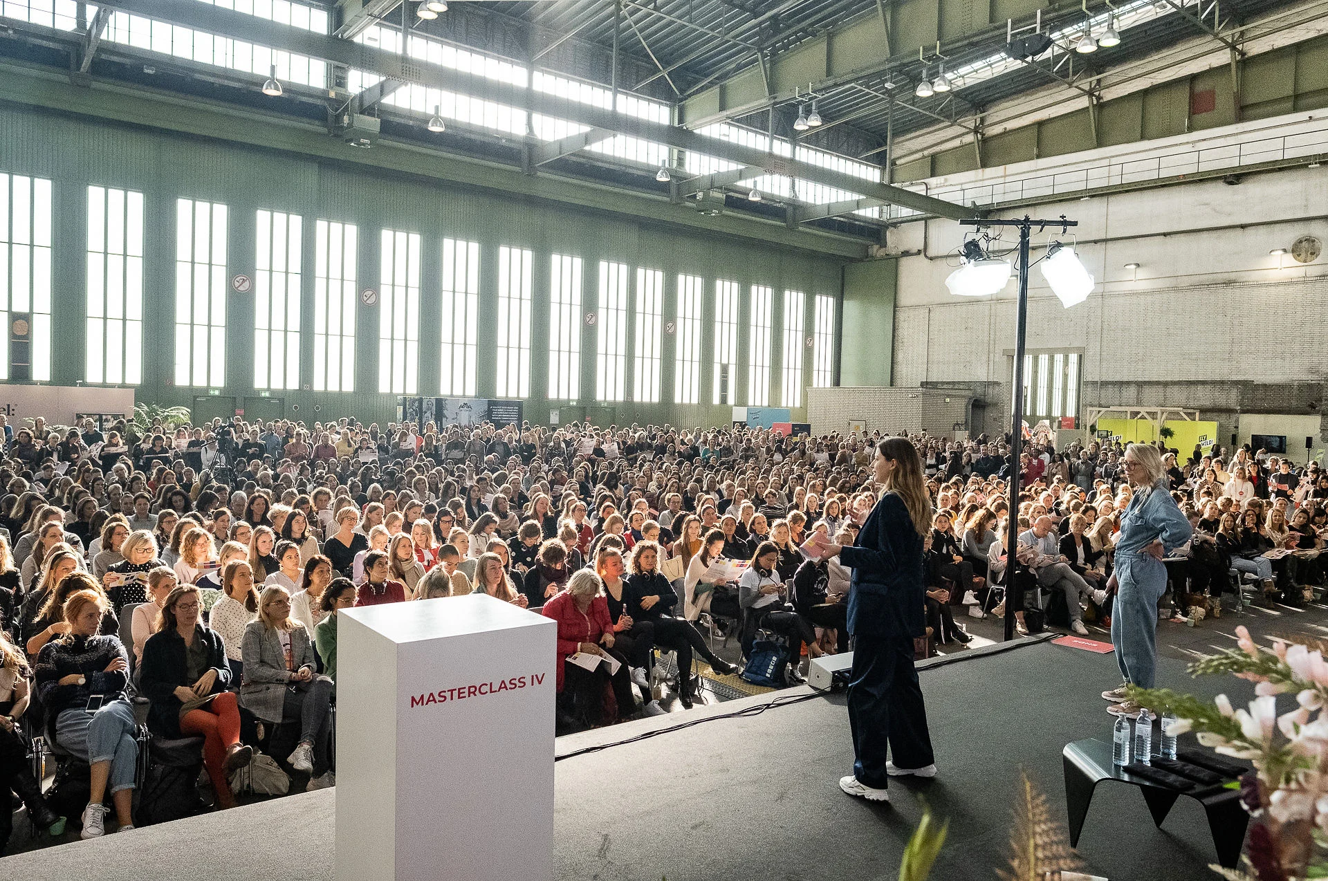 Speaker on the masterclass stage facing a packed audience of thousands in the Tempelhof hangar at Female Future Force Day.