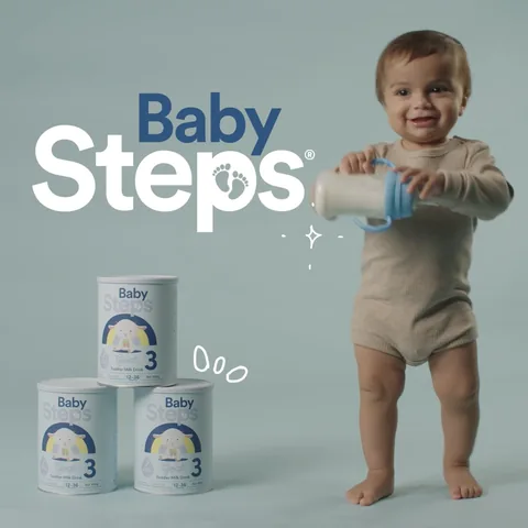 A toddler stands with a cup beside three tins