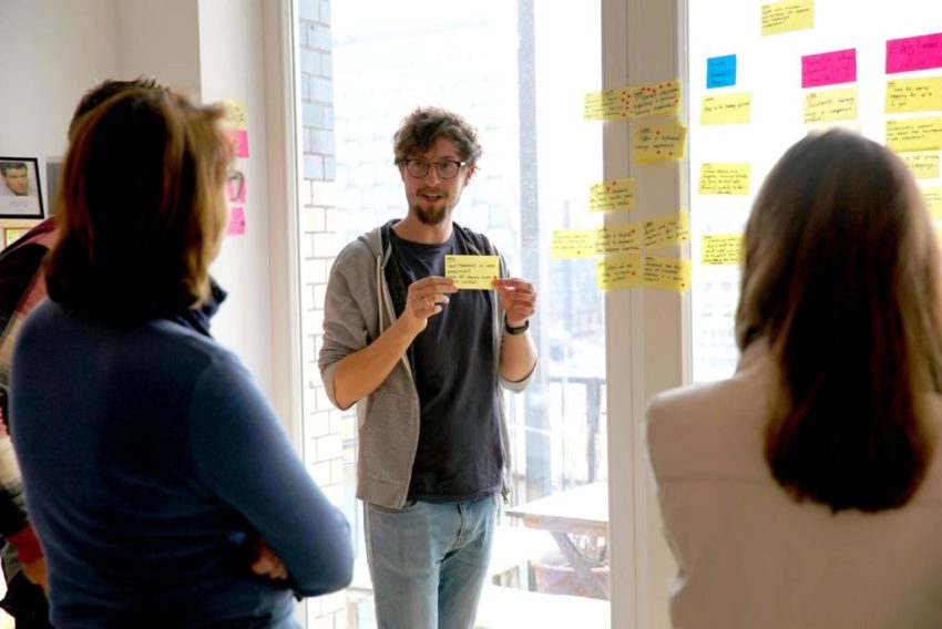 Facilitator holding up a sticky note while explaining an idea to a small group in a workshop