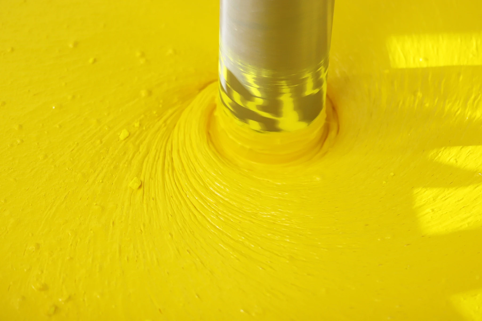 Bright yellow ink or coating being blended into a swirling vortex by a mixer.
