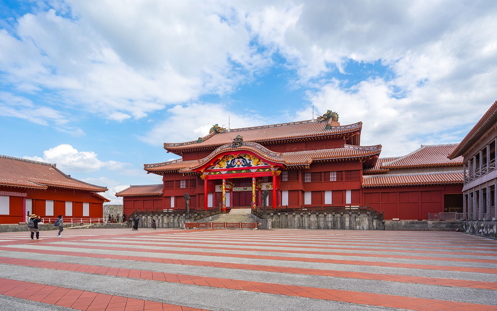 Το Κάστρο Σούρι στην Οκινάουα, Ιαπωνία, με την παραδοσιακή κόκκινη αρχιτεκτονική και τους τουρίστες που εξερευνούν τον χώρο.