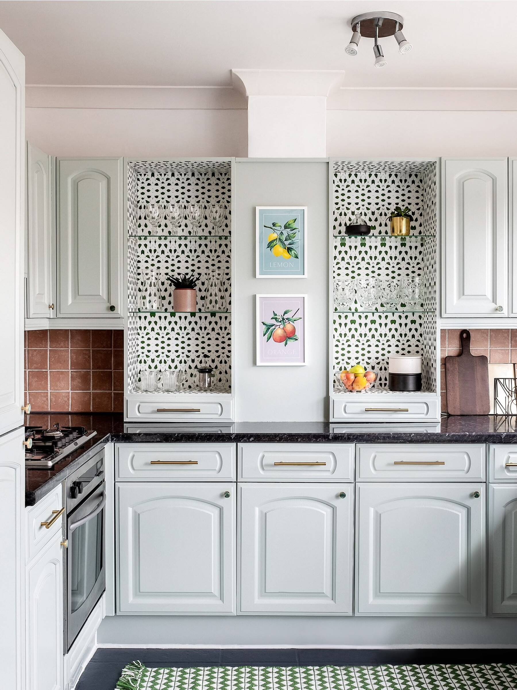 Bright and playful kitchen by Atelier Akuko featuring sage green cabinets, brass handles, and charcoal tile floor, showcasing a budget-friendly transformation
