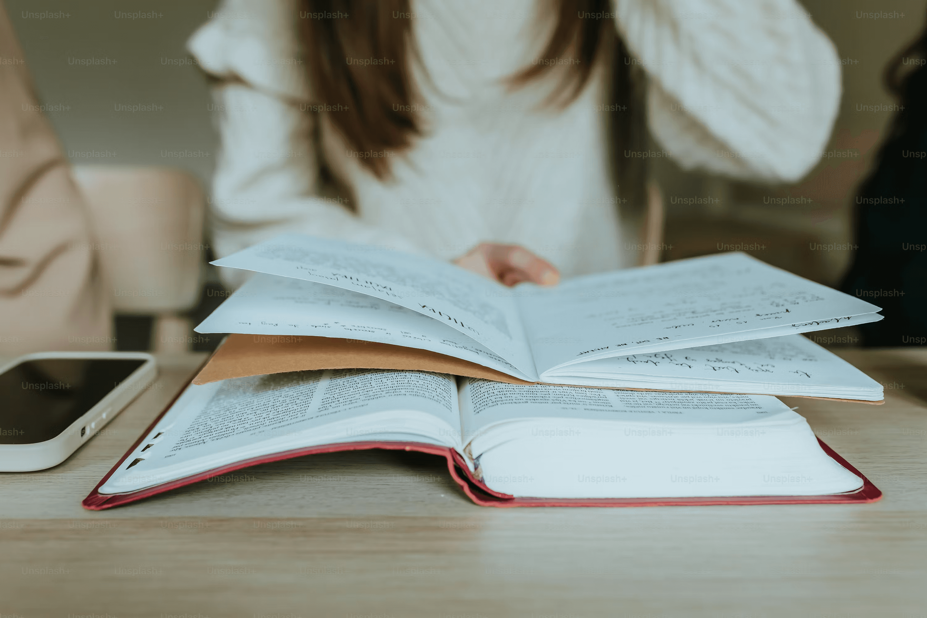 High school student writing a literature review at a desk surrounded by academic journals and research papers