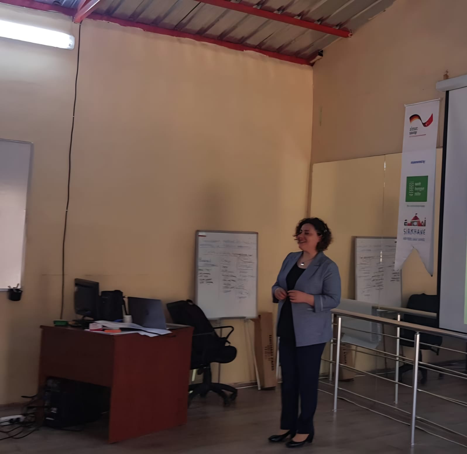 Smiling young woman with long hair standing against a dark green background, holding a finger to her chin.