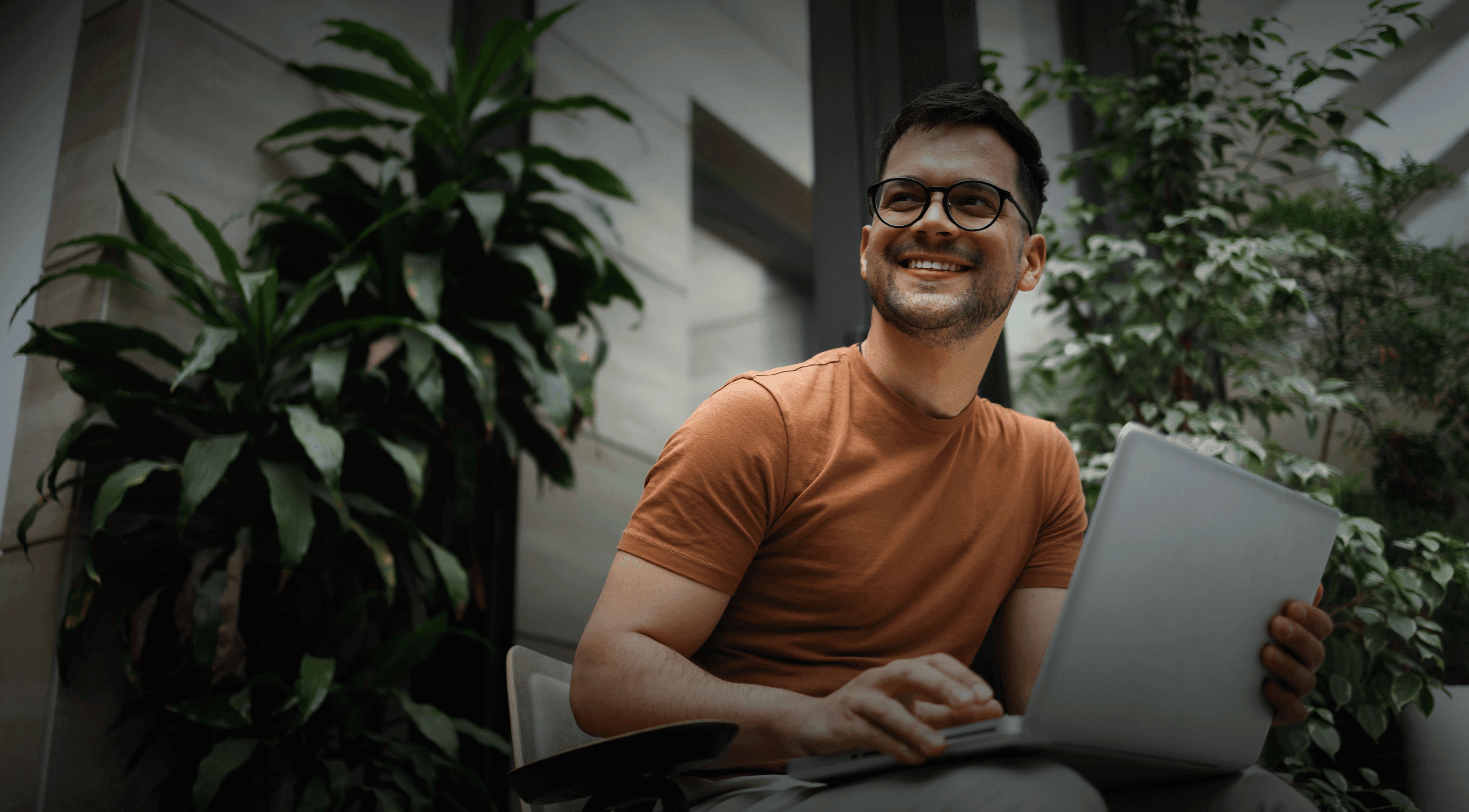 Young business man in orange t-shirt sitting on a chair smiling with a laptop