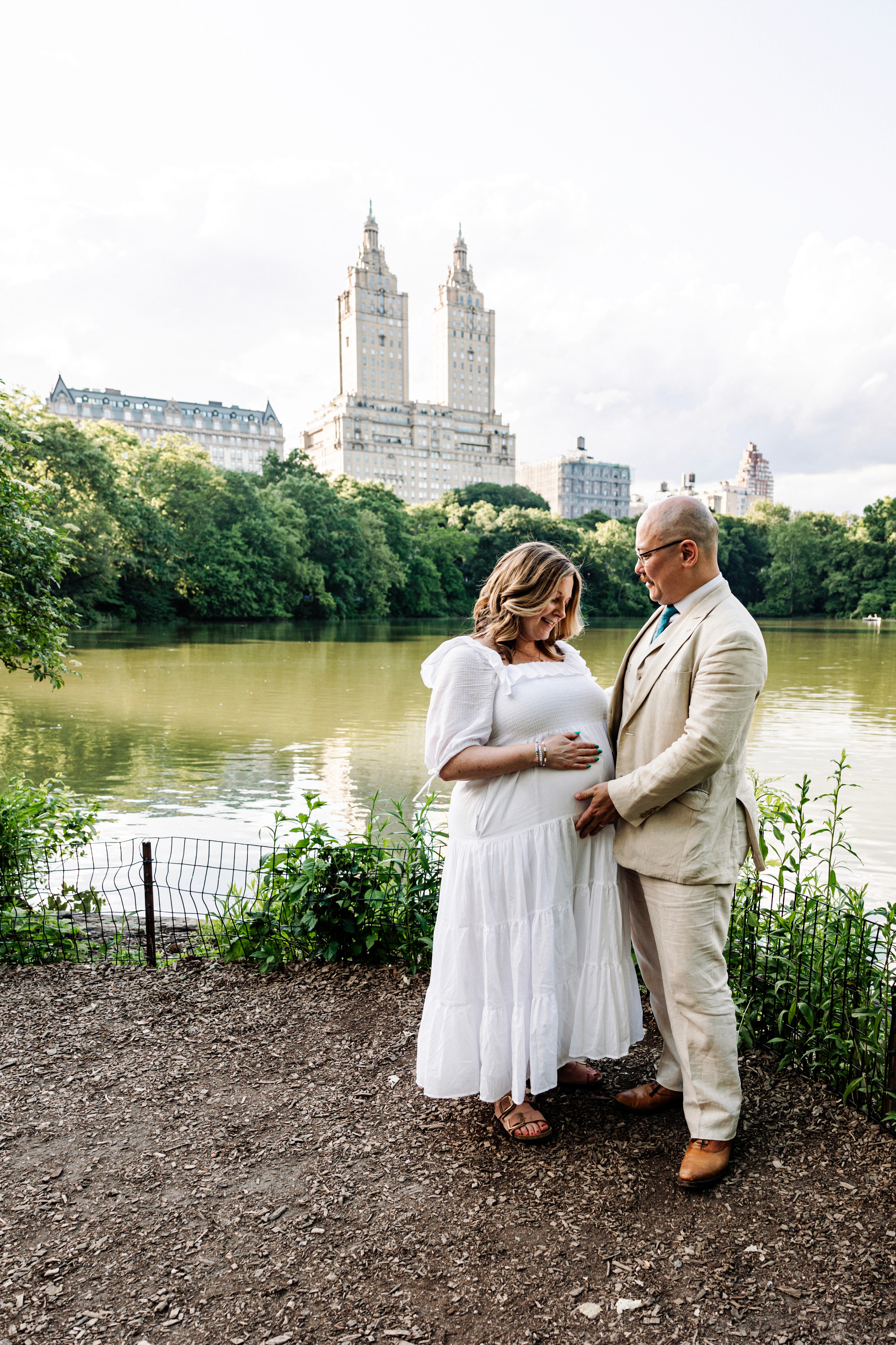 Glowing couple at nine months pregnant surrounded by lush greenery with the iconic San Remo building on Central Park West as a stunning backdrop — elegant, natural maternity photography by Lizz Spano Photography, New York City maternity photographer.