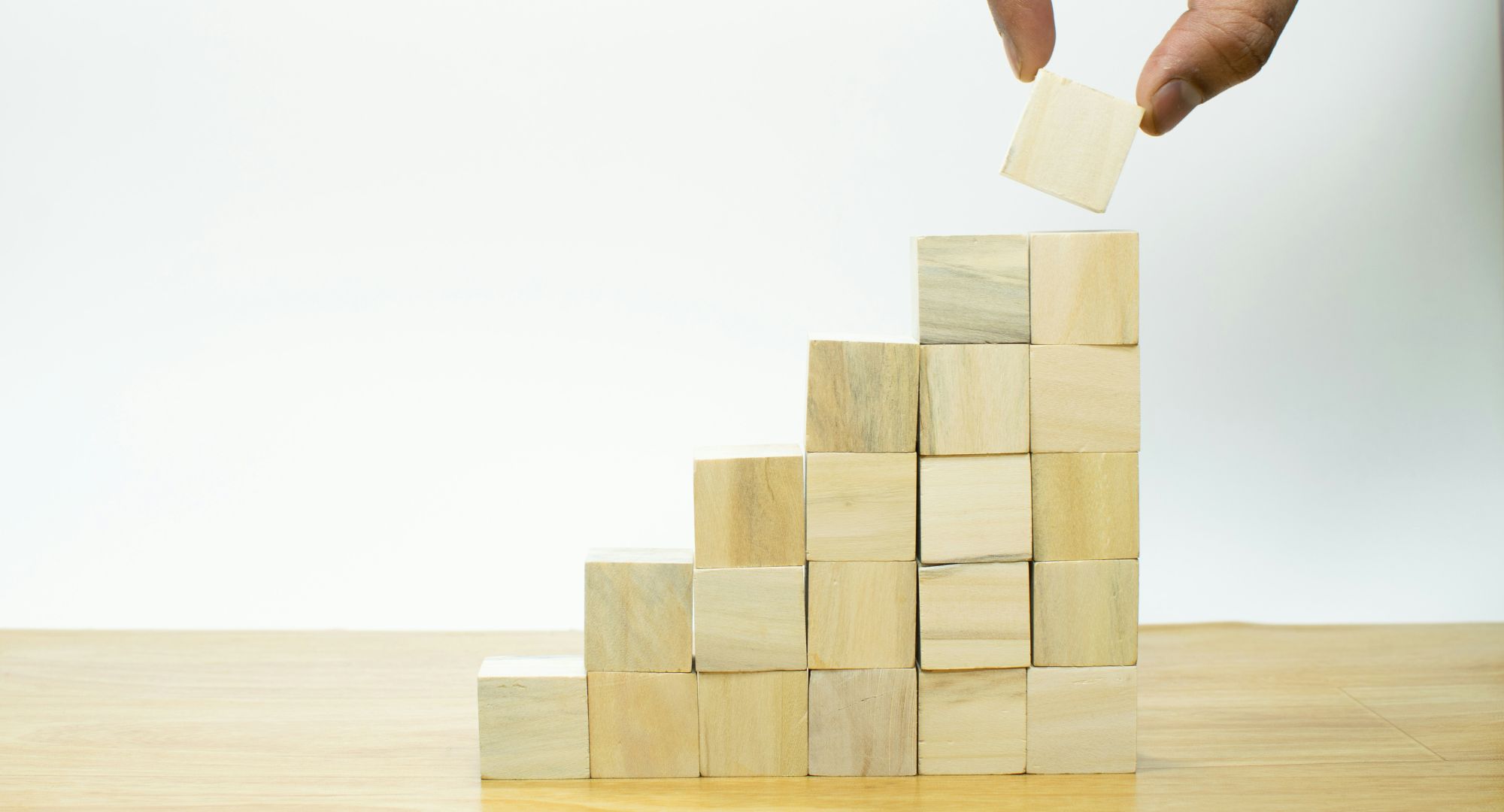 pessoa colocando um cubo de madeira em uma pequena escada feita de várias dessas peças, fundo branco