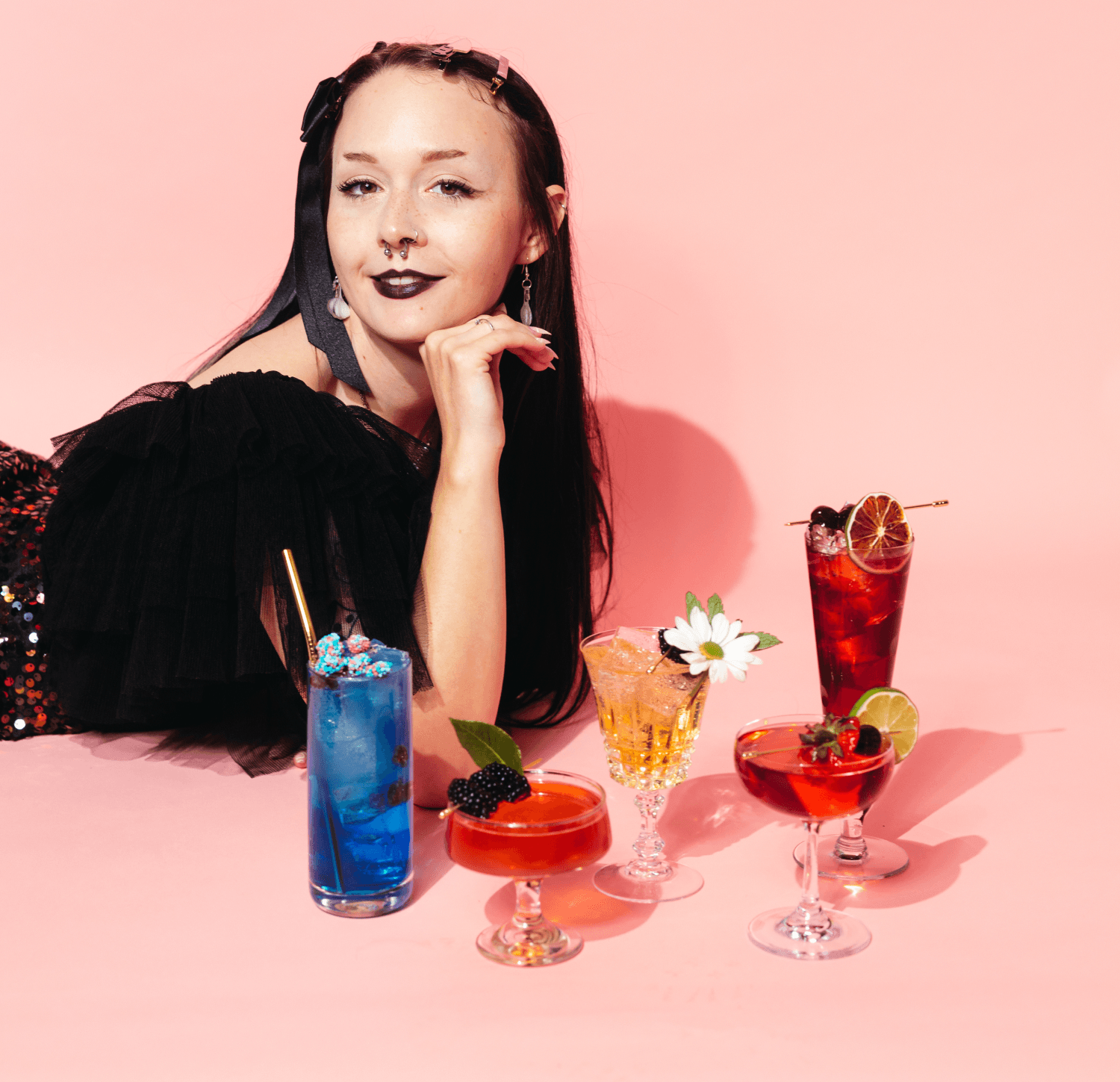 Sophie Liffick, owner of So Curious Co, poses with her non-alcoholic drinks on a pink background