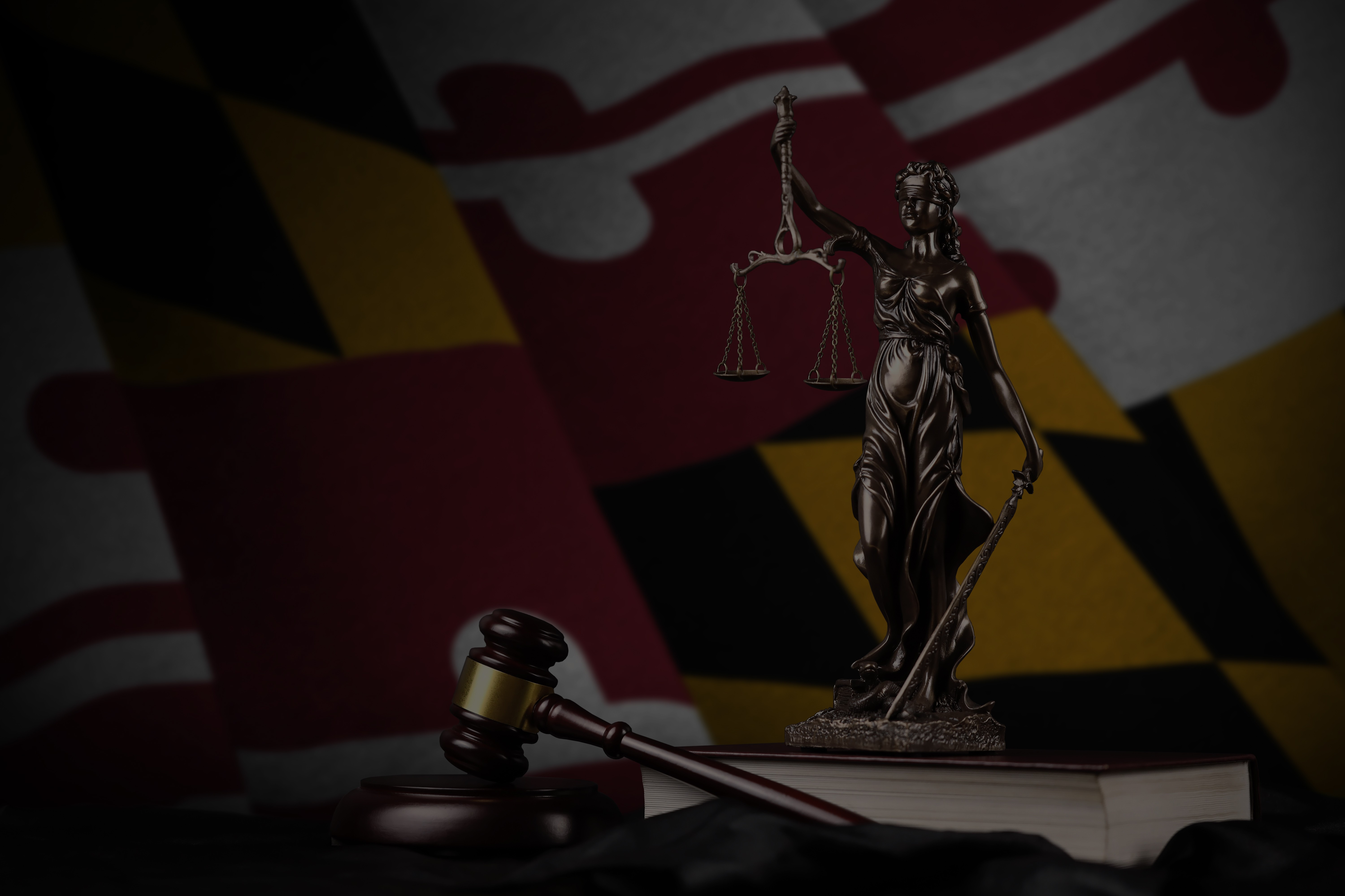 A bronze statue of blindfolded lady justice holding scales with the Maryland state flag in the background