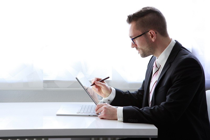 Geschäftsmann sitzt am Tisch mit Tablet und schreibt auf dem Display