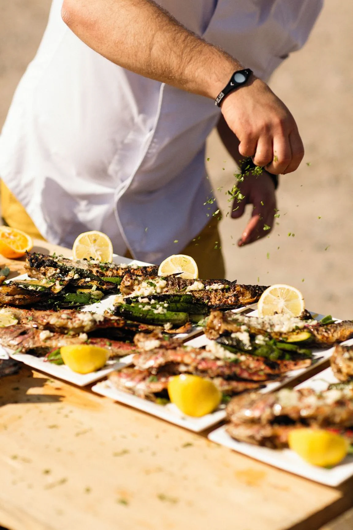 Chef preparing grilled seafood with lemon slices at an outdoor beachside BBQ station.