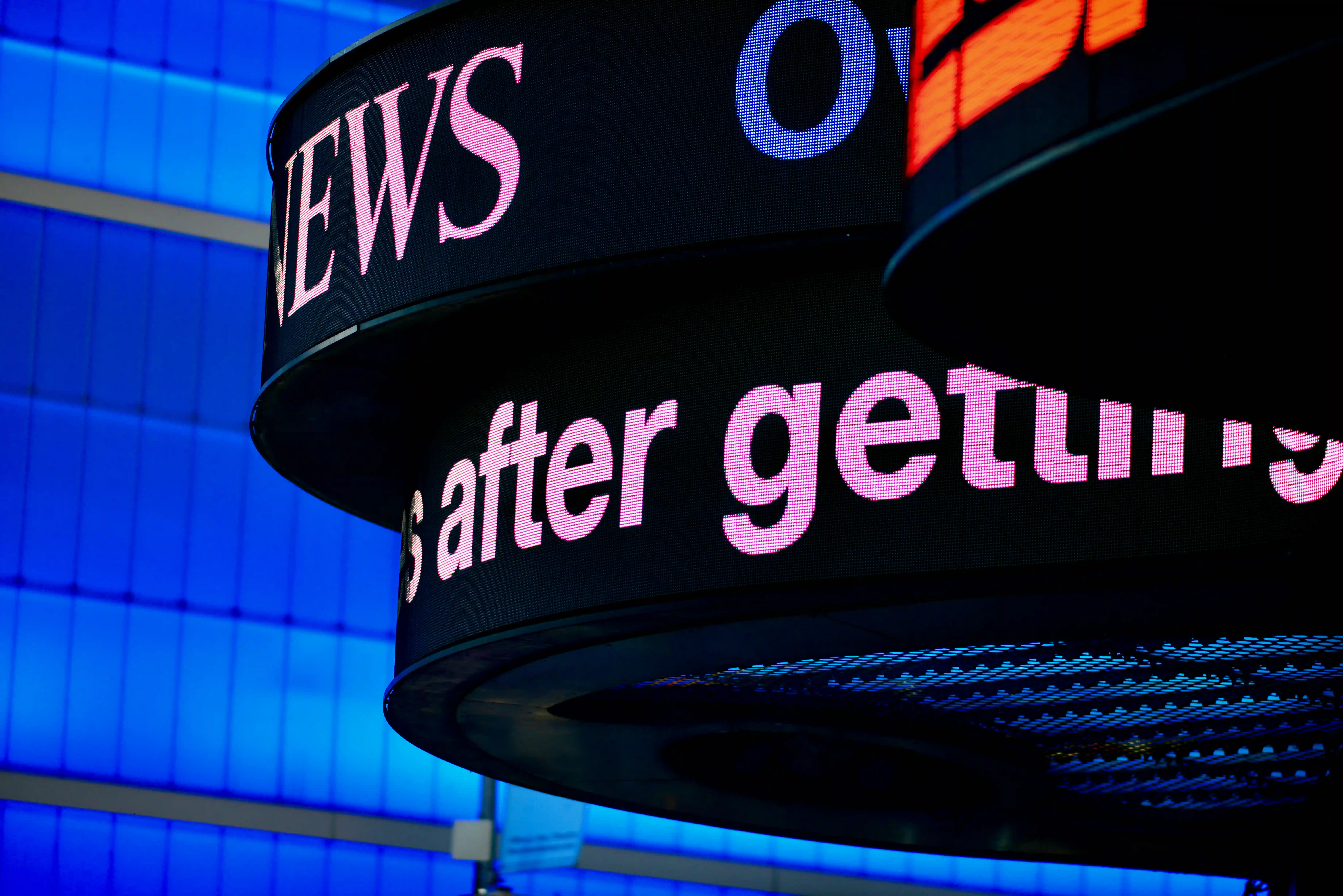 A digital news ticker displaying breaking headlines against a blue building, representing real-time media and financial market updates.