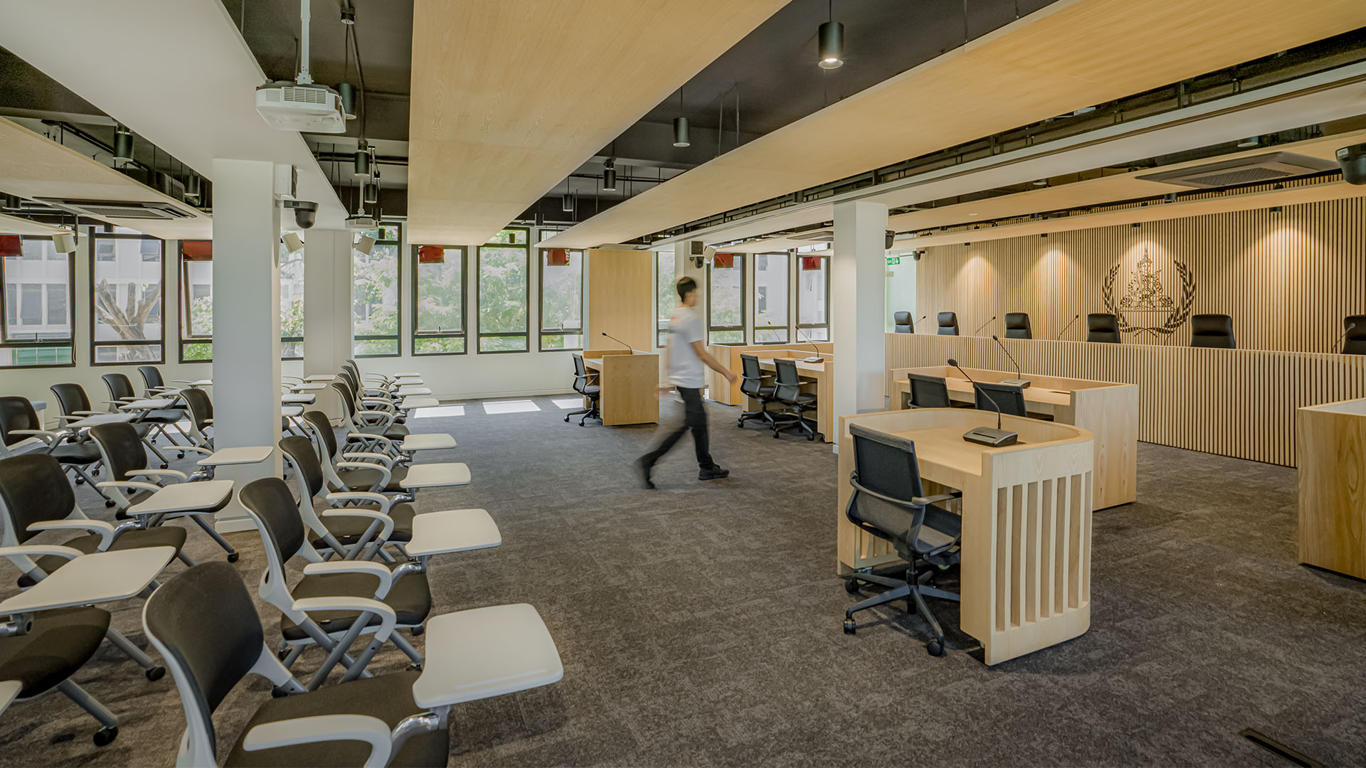 A wide view of the ECCC Courtroom in Phnom Penh, highlighting the light wooden slatted desks, integrated microphones, and ergonomic chairs.