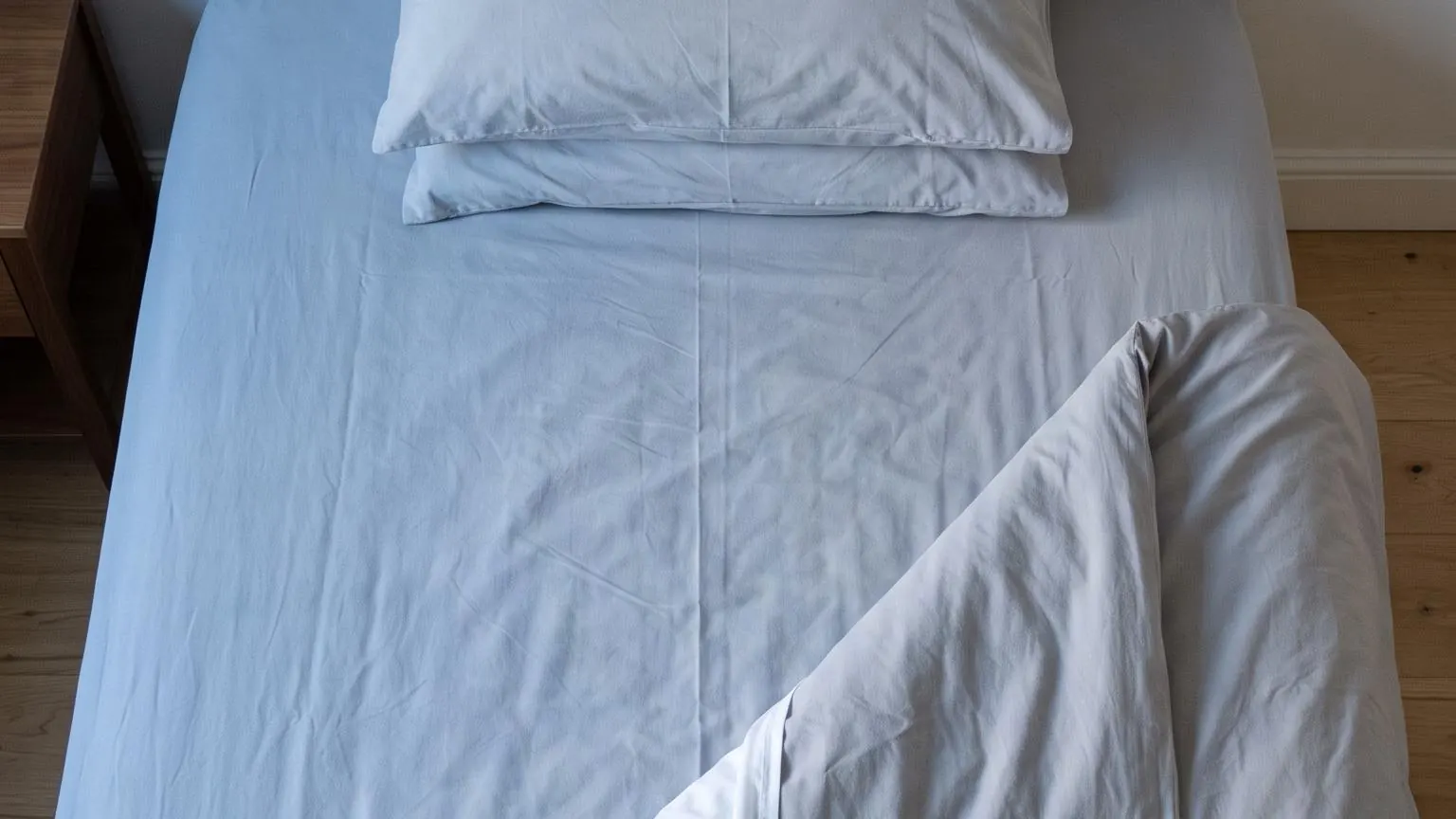 Seen from above, a neatly made bed with one corner turned back in cool light before sunrise