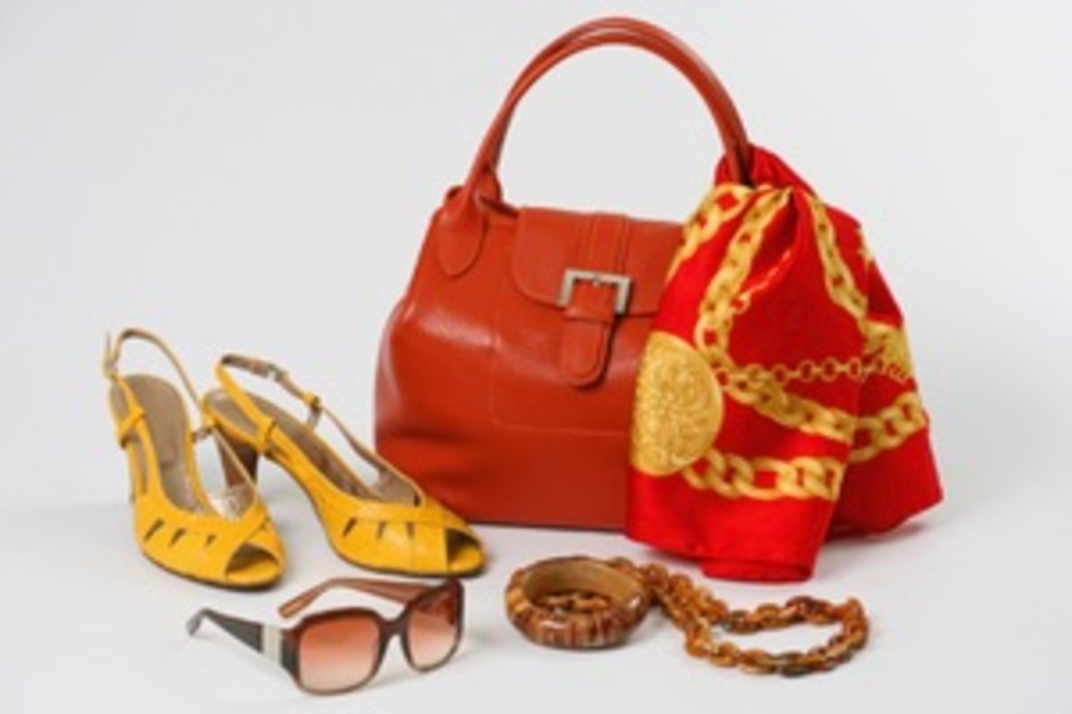A flat lay of fashion accessories featuring a bold red handbag, patterned scarf, yellow heels, brown sunglasses, and jewelry, highlighting vibrant color coordination for a stylish ensemble.