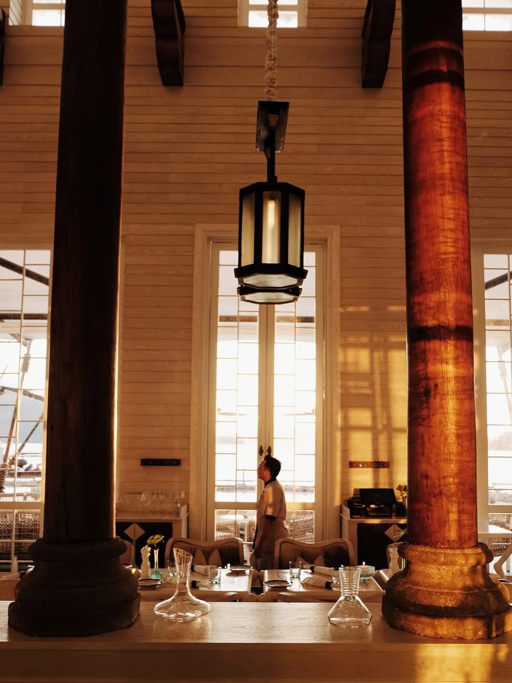 Interior view of a dining area at The St. Regis, Langkawi, showcasing elegant furnishings and warm lighting, with a staff member walking through.