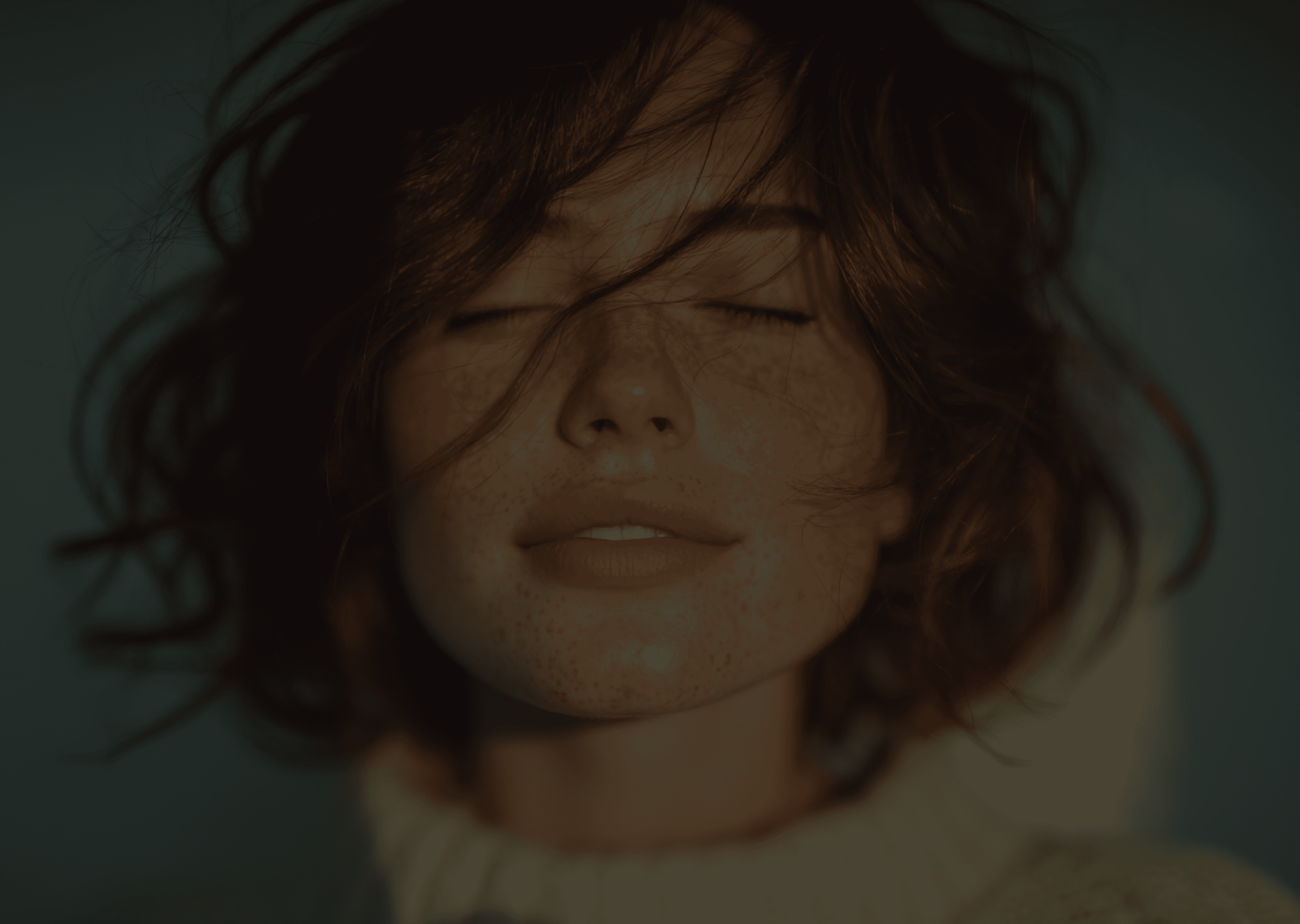 Close-up of a woman with her eyes closed, her hair covering part of her face. She appears serene and peaceful.