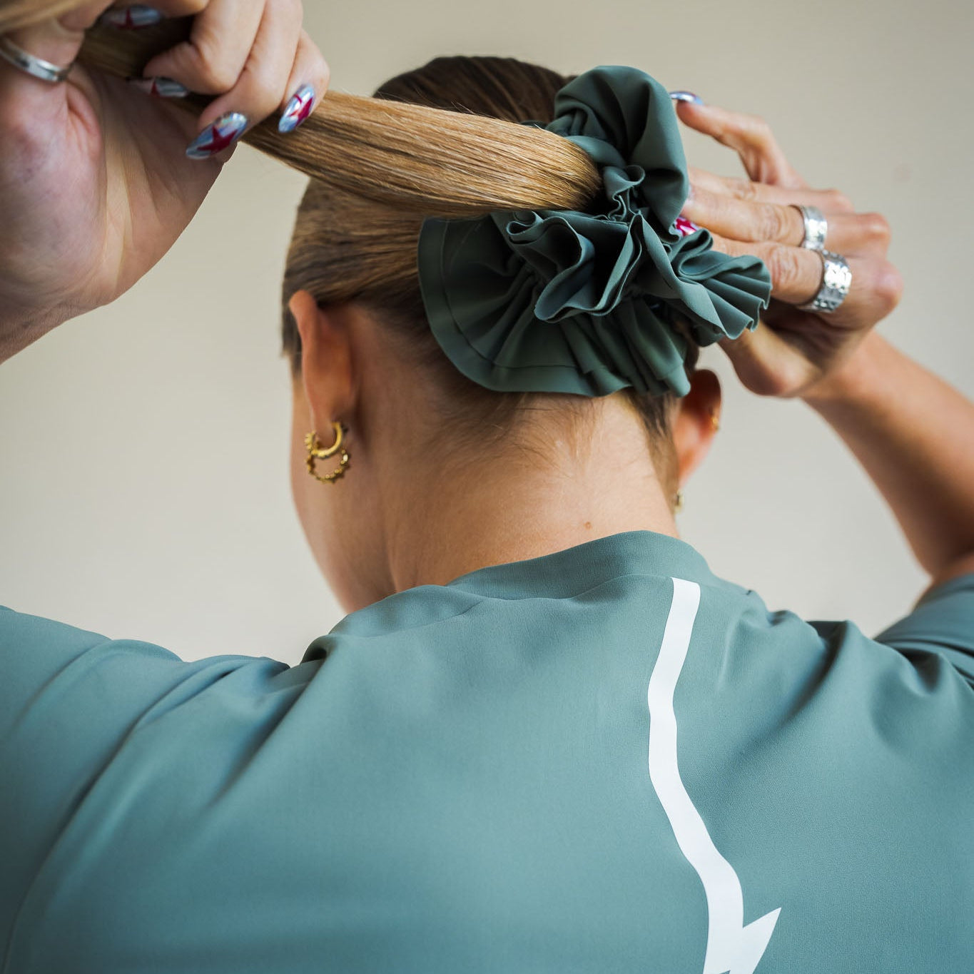 Cyclist tying ponytail with LUCA Uplift scrunchie in matcha, arms raised