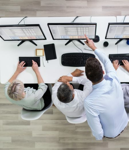 Group of people working on computers pointing at screen and data diagrams