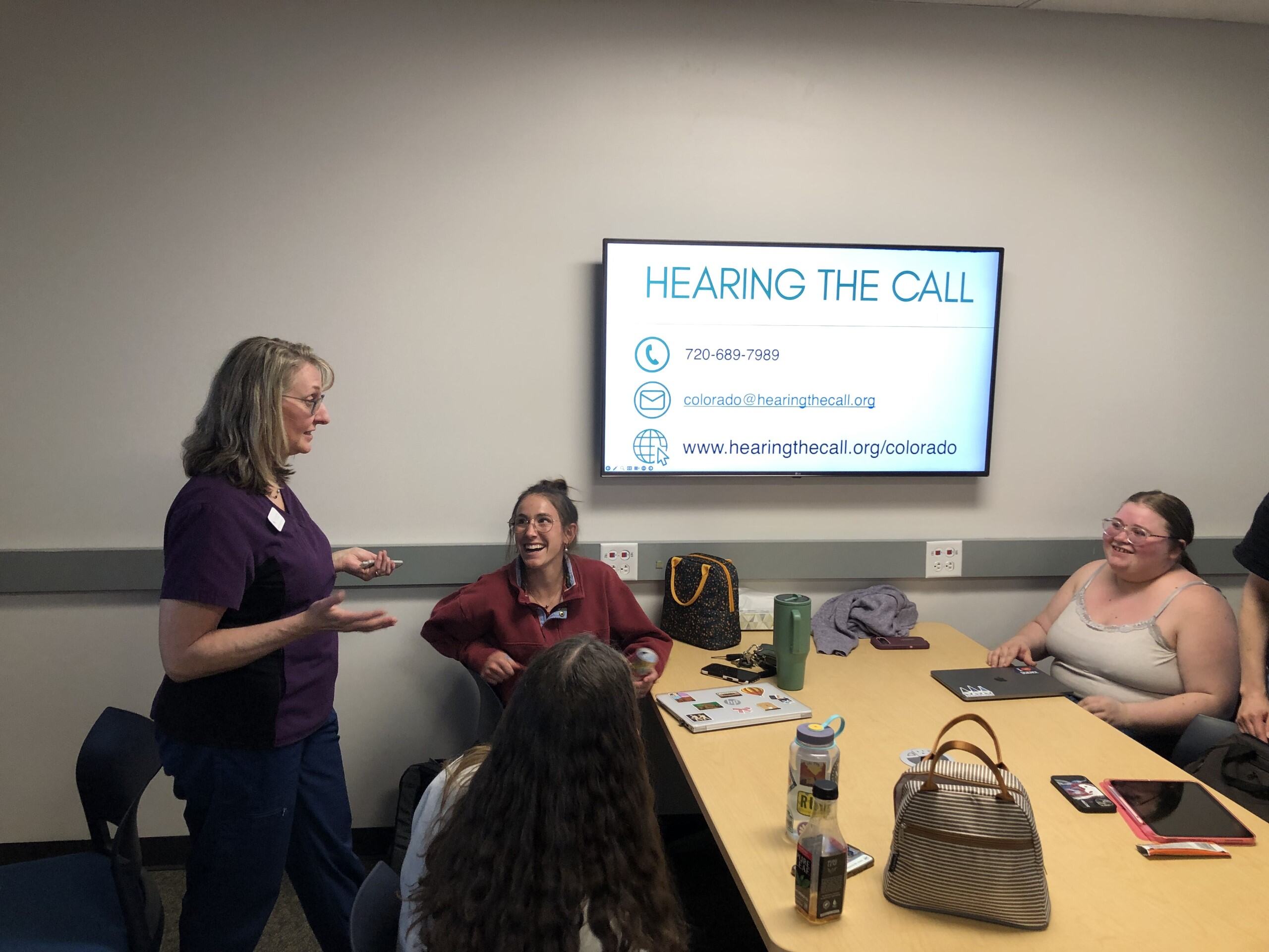 Two people are engaged in conversation outdoors; one is seated while the other is leaning closer.