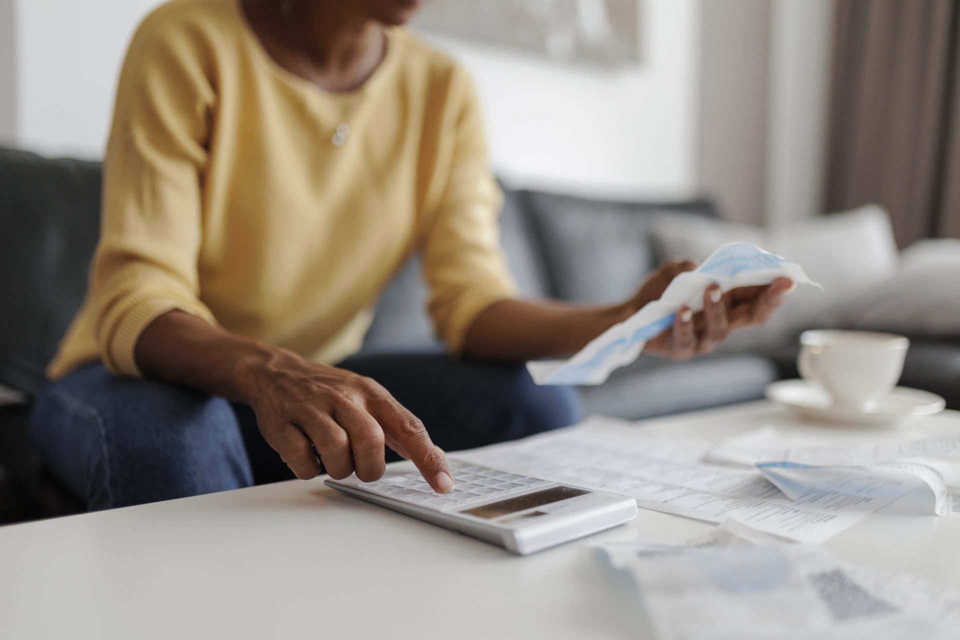 Person using a calculator with bills and a cup of coffee.