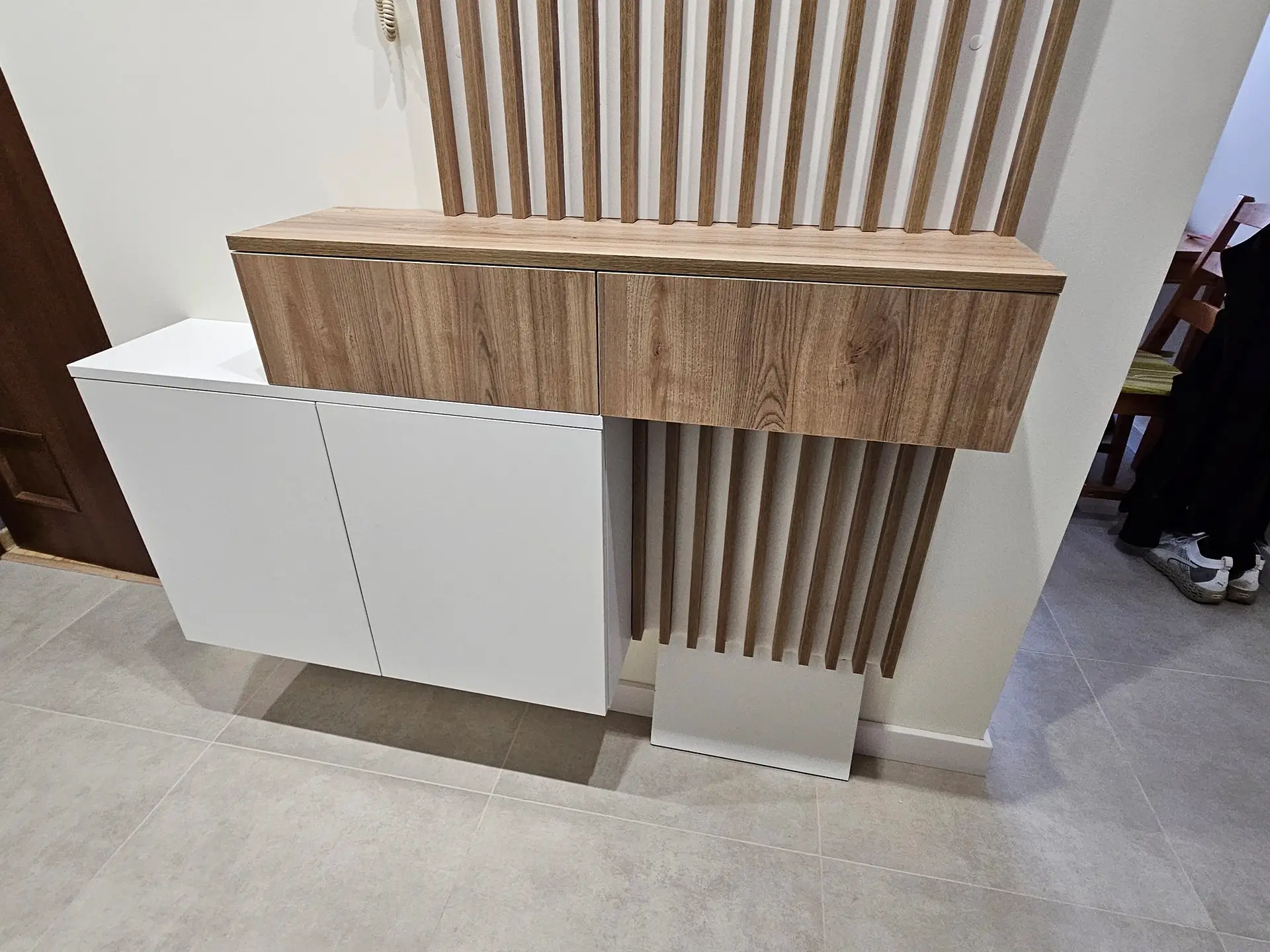 Nowoczesna konsola przedpokojowa z drewnianymi lamelami i szafkami w kolorze białym i drewna.