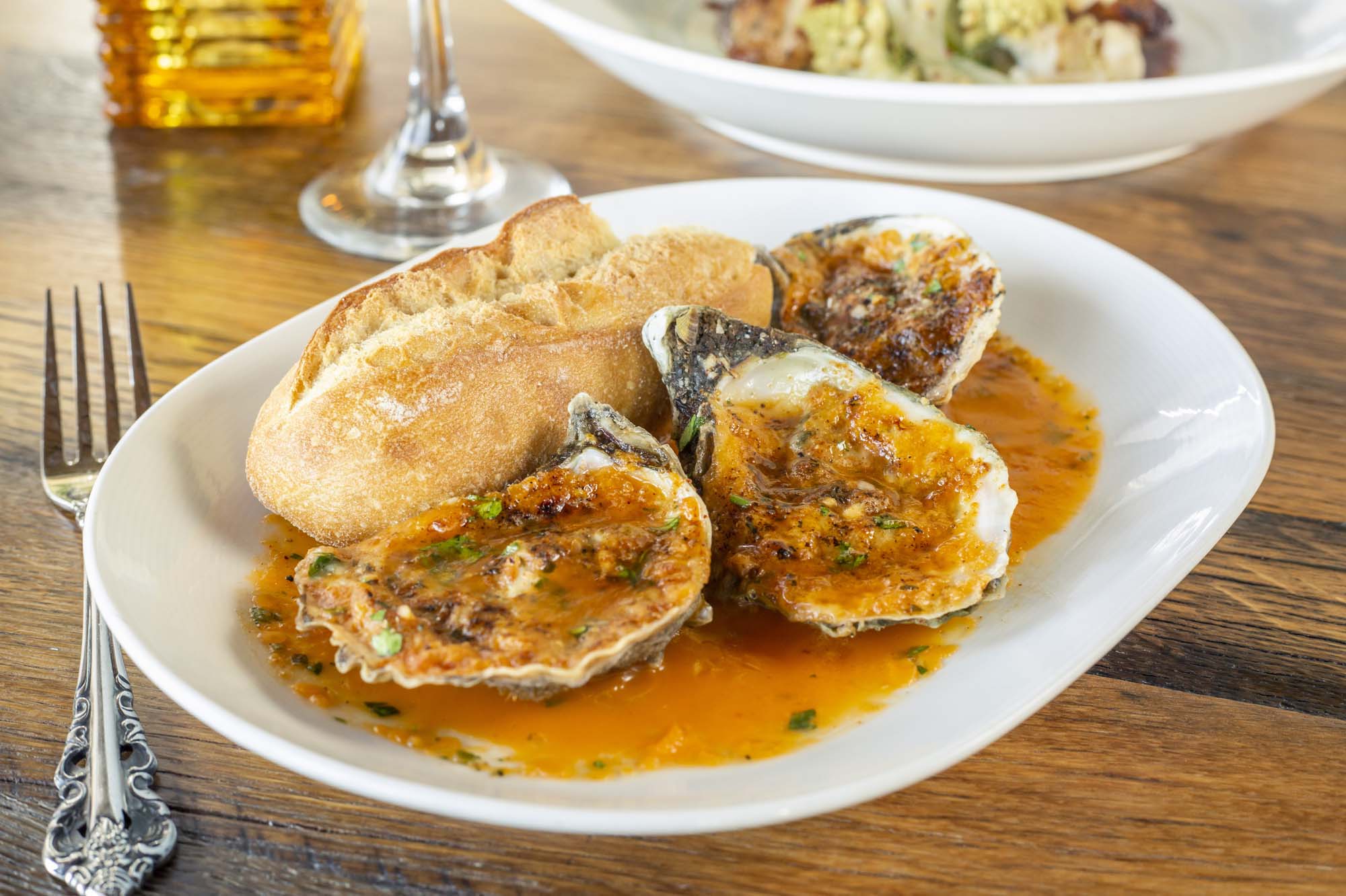 Chargrilled oysters with bread in a buttery sauce on a white plate at The Pearl Short North