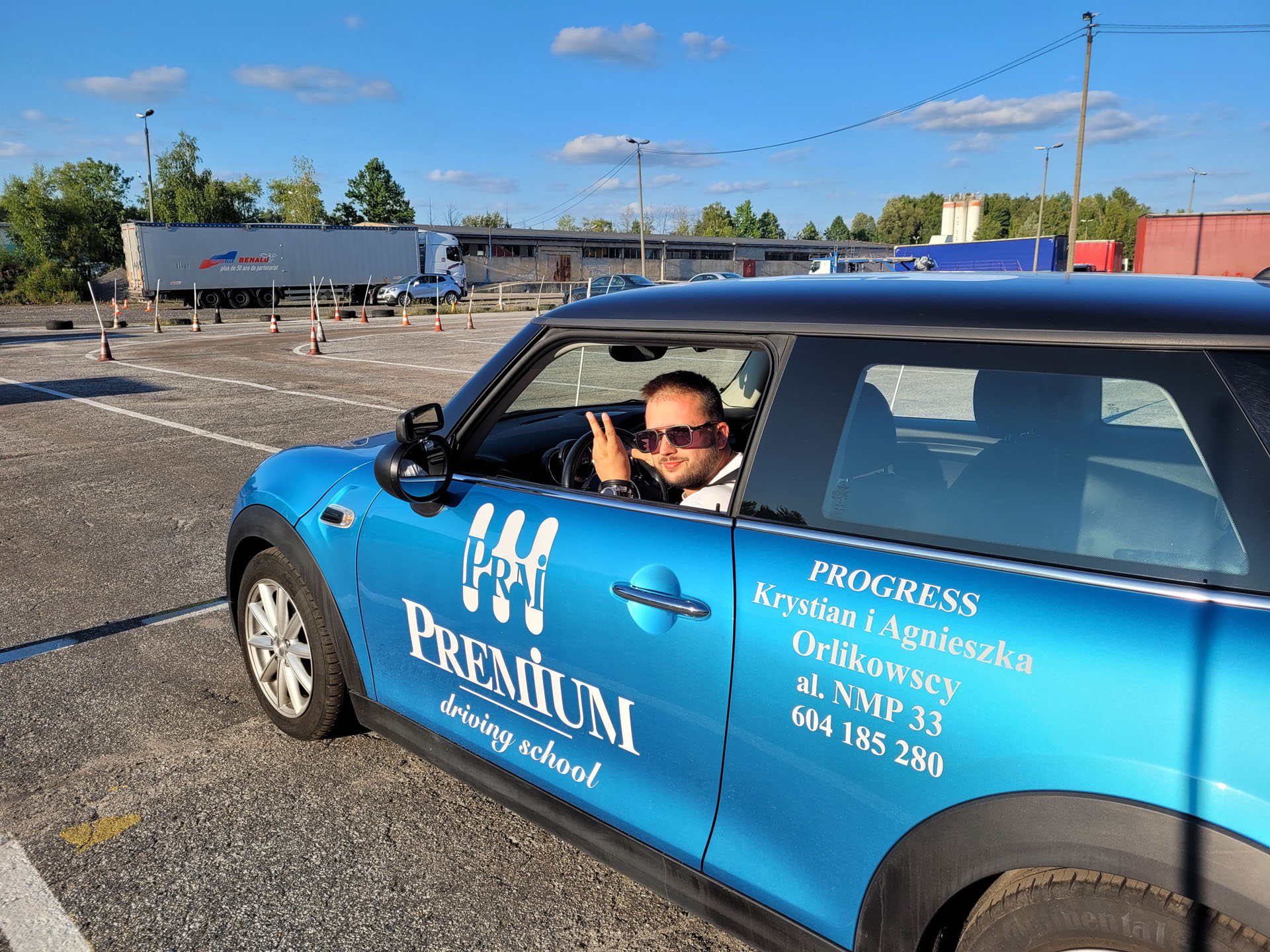 Niebieski samochód OSK Premium Driving School na placu manewrowym.