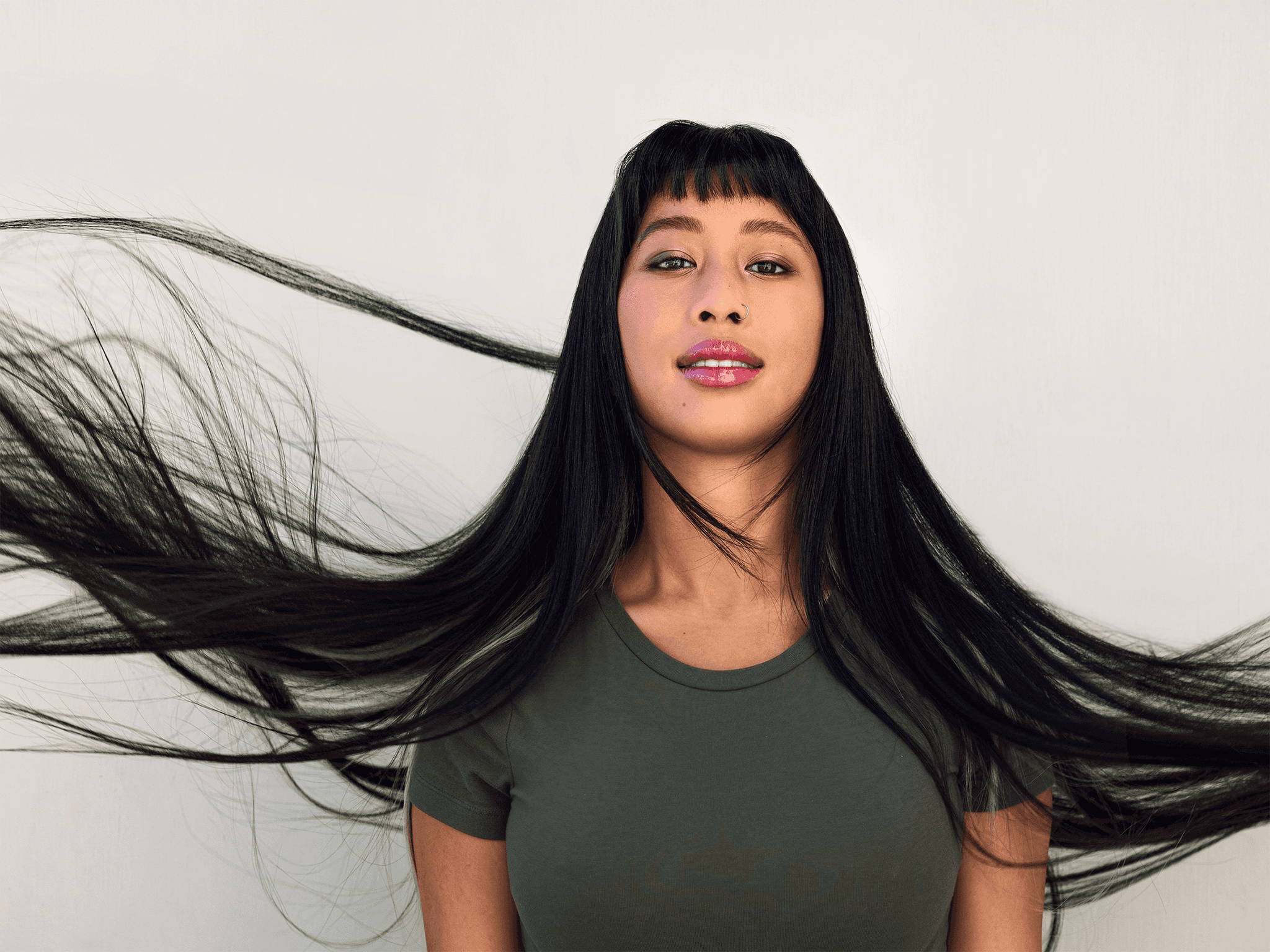 Portrait from the chest up of the subject with long black hair floating in the wind. She is looking strange at us with confident and a soft smile